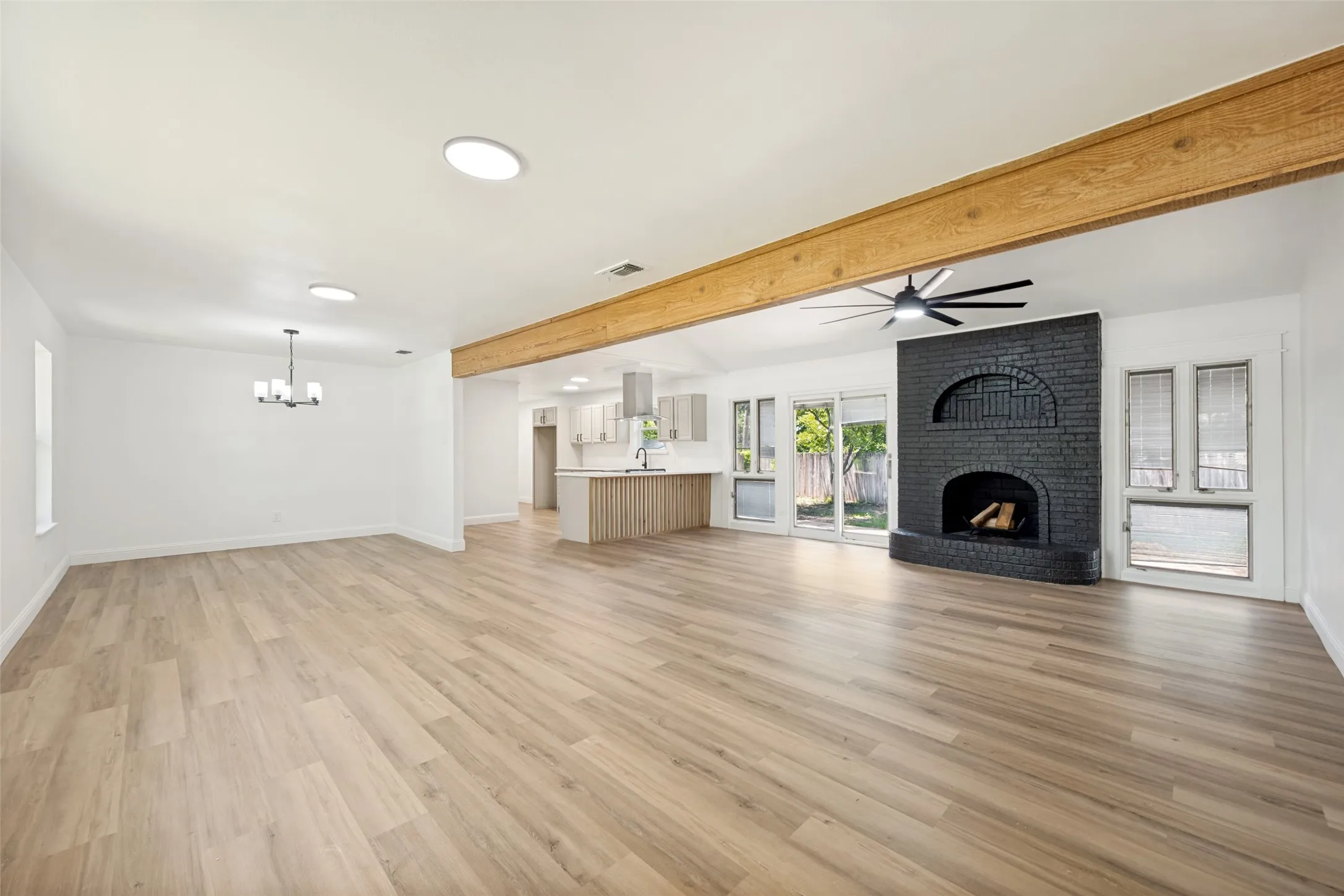 Spacious living area featuring wood-finish flooring, a prominent black brick fireplace, and exposed wood beam accents