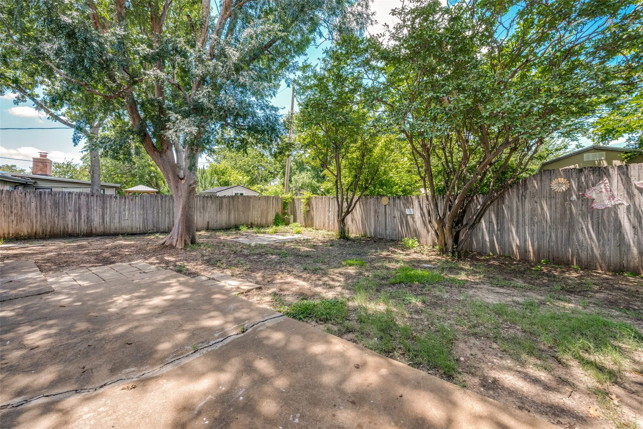 Private backyard featuring mature trees, a perimeter wood fence, concrete patio, and natural landscaping