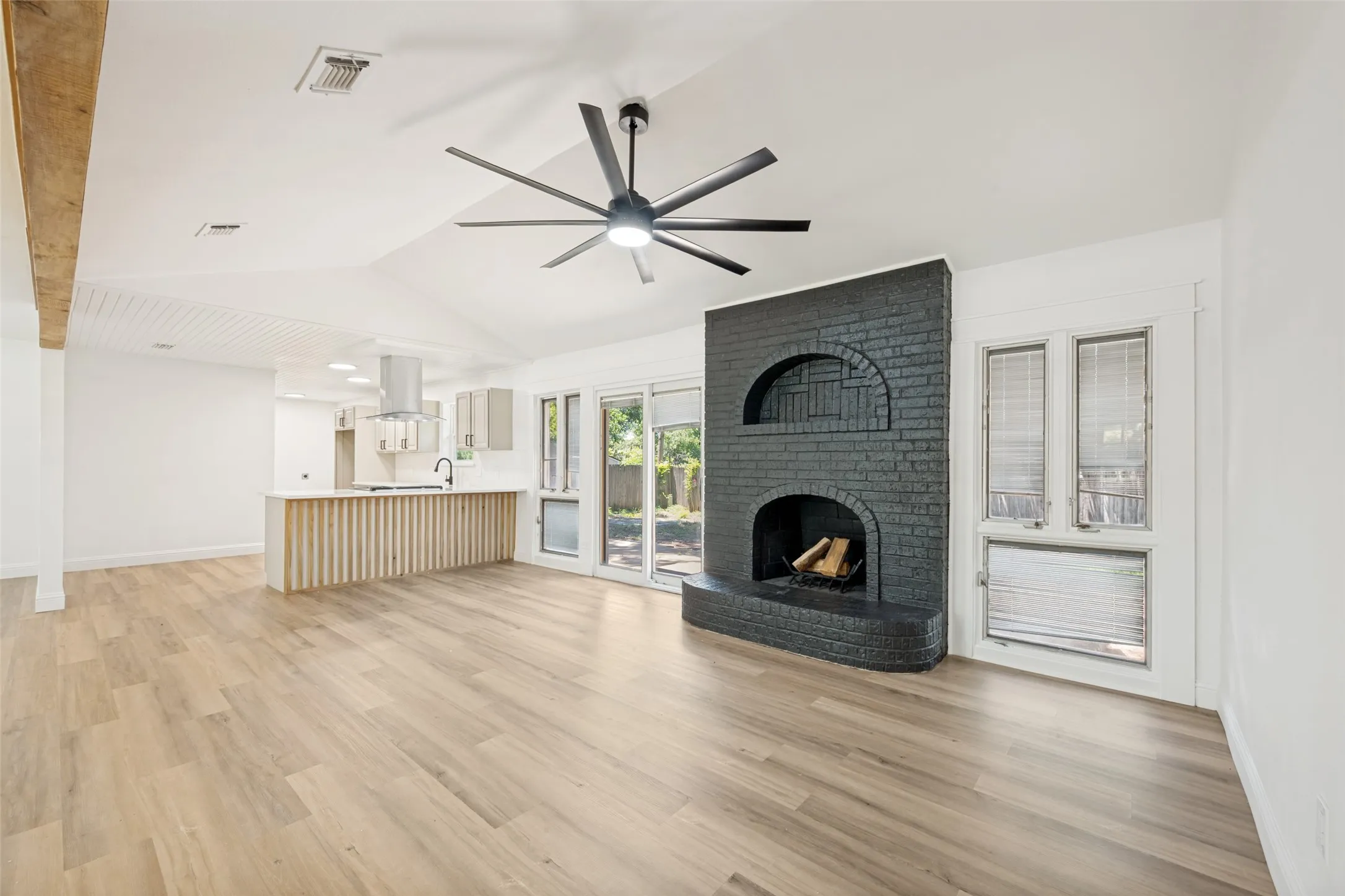 Spacious living area featuring a dark brick fireplace, light wood-finish flooring, and a contemporary ceiling fan