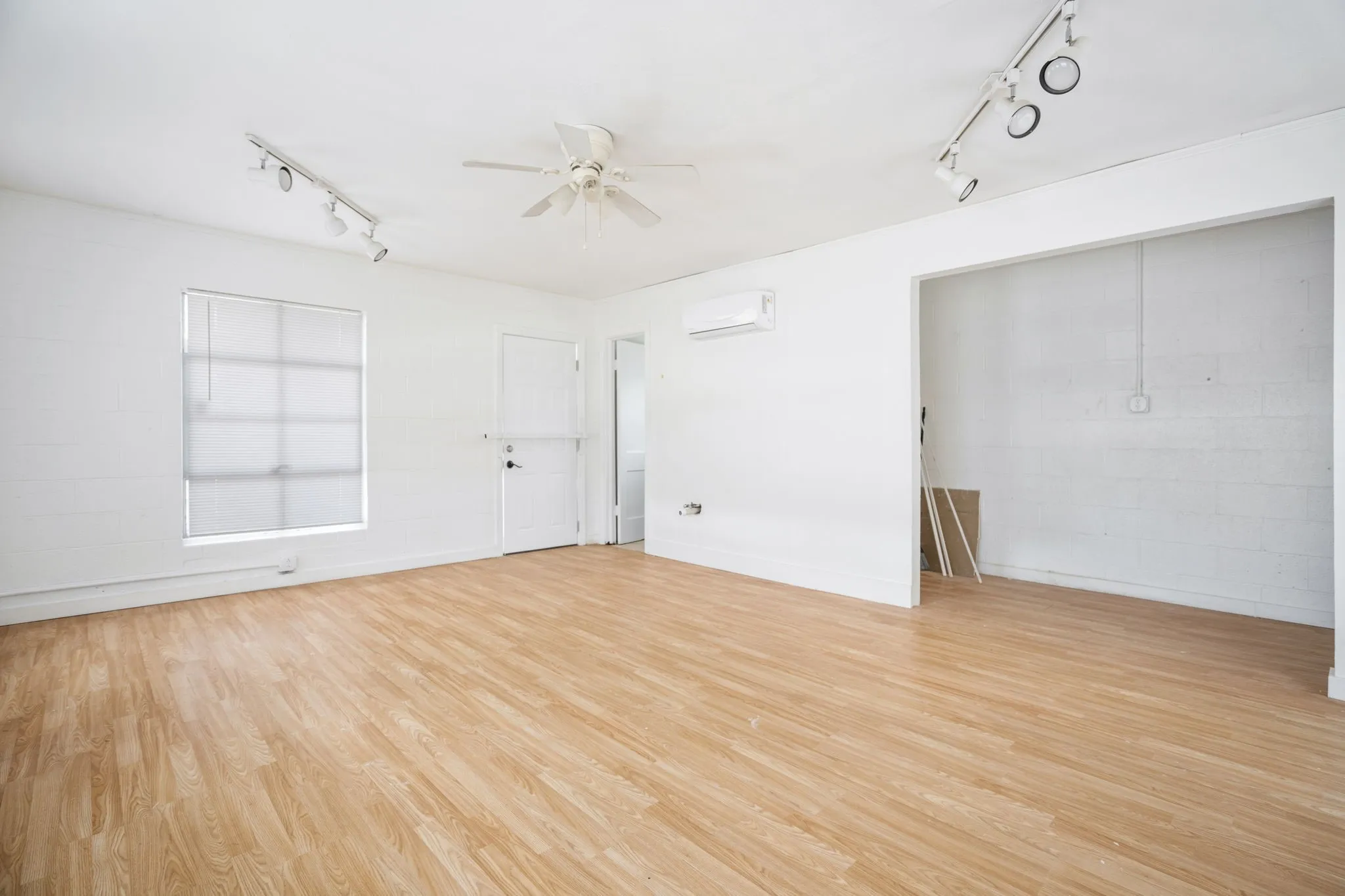 Spacious room featuring light wood-finish flooring, white walls, and a window with blinds
