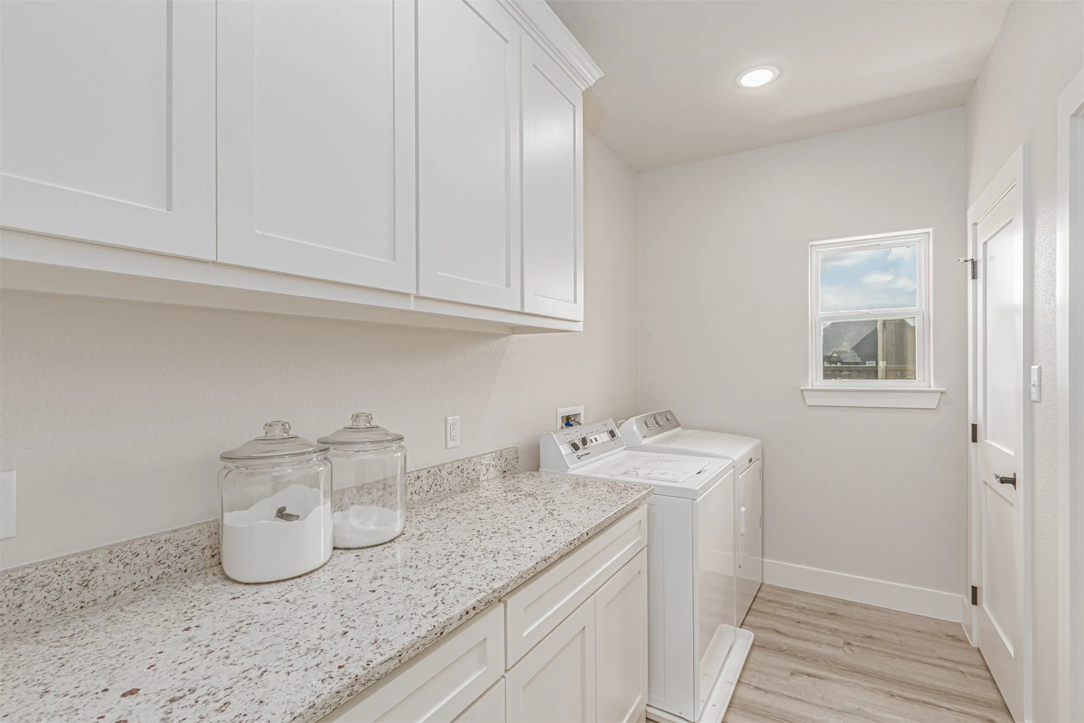 Utility room featuring white shaker cabinetry, speckled countertop, window with white trim, wood-finish flooring, and recessed lighting