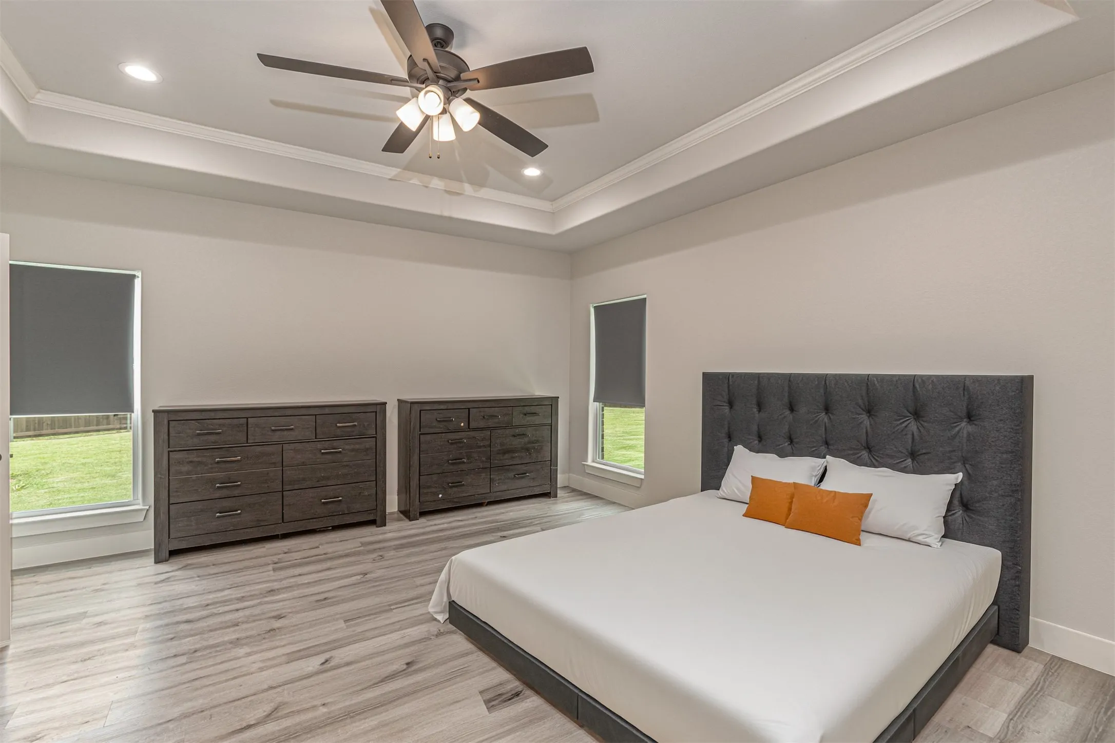 Spacious room featuring tray ceilings with recessed lighting, a ceiling fan, and wood-finish flooring