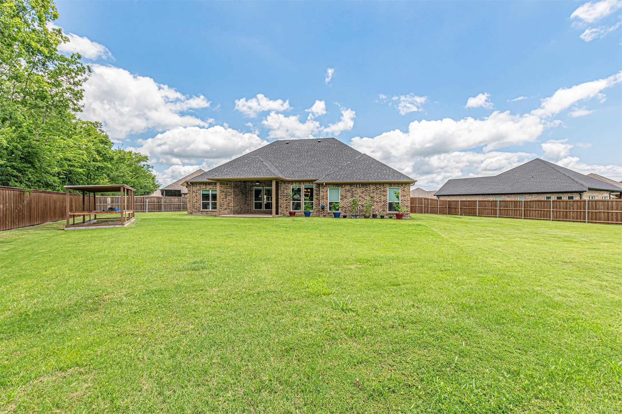 Expansive backyard featuring a lush lawn, a covered wooden pergola, a full privacy fence, and a brick exterior with multiple windows