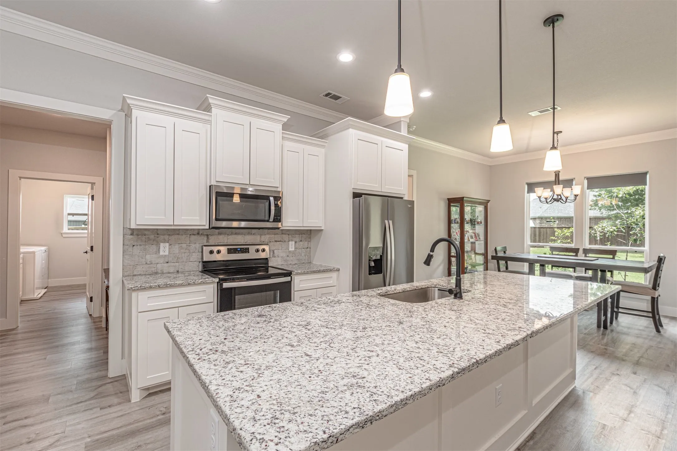 Kitchen featuring a large island with a stainless steel sink and matte black faucet, white shaker cabinetry, stainless steel appliances, speckled countertops, and wood-finish flooring