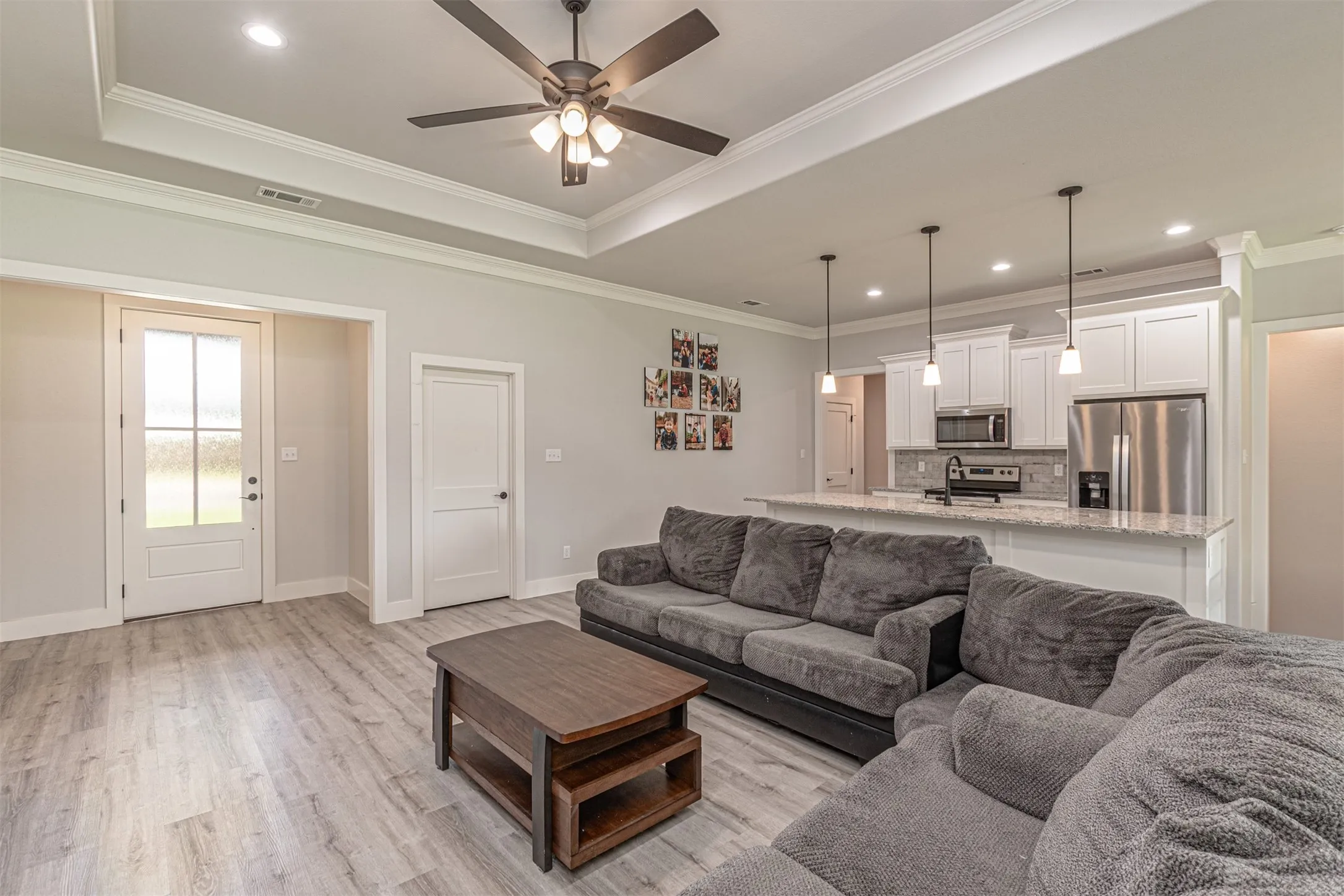 Open-concept living area with wood-finish flooring, tray ceiling, recessed lighting, and a modern ceiling fan