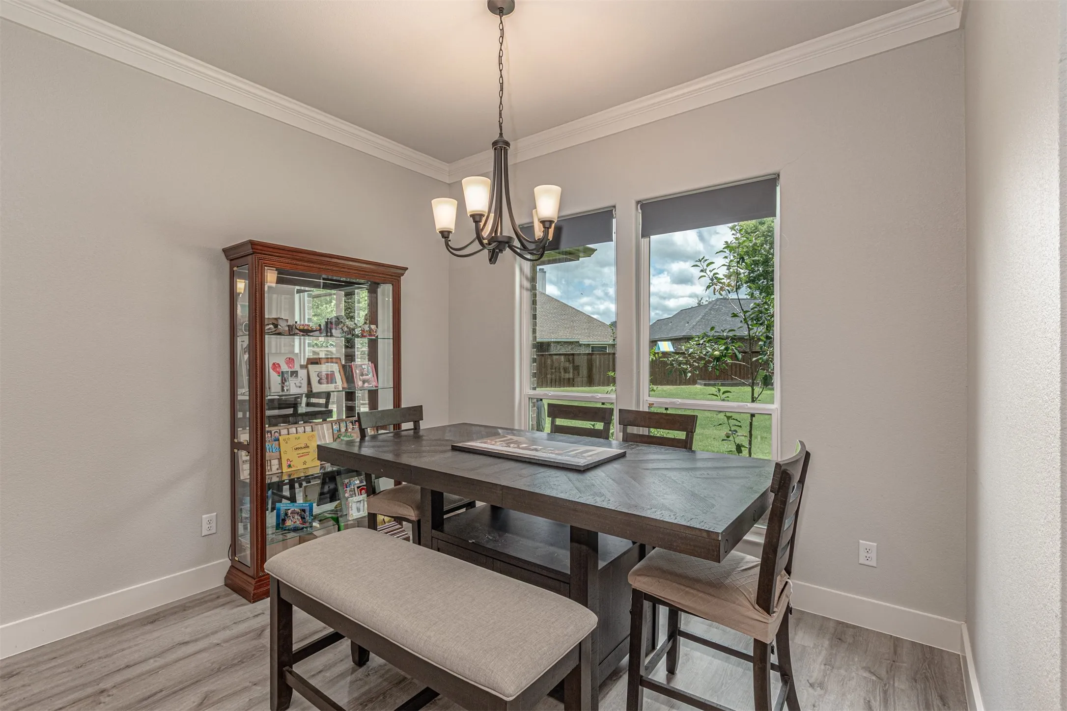 Dining area featuring light gray walls, white crown molding, wood-finish flooring, and multiple windows providing natural light