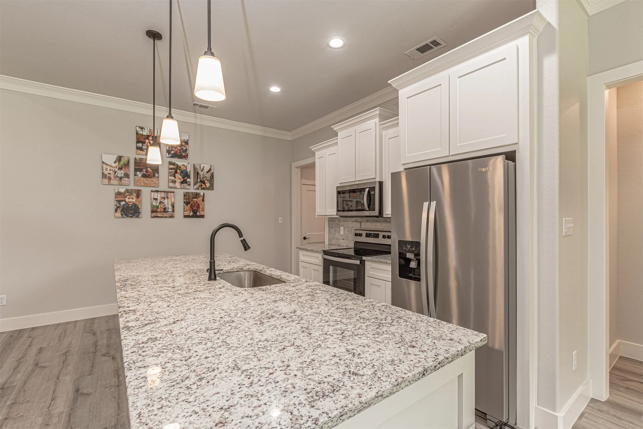 Kitchen featuring a large island with a stainless steel sink and matte black faucet, granite countertops, white shaker cabinetry, and stainless steel appliances