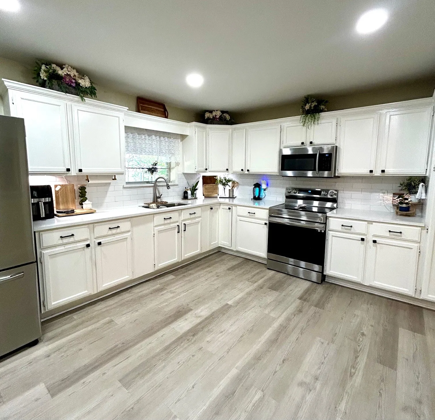 Kitchen featuring appliances with stainless steel finishes, white cabinets, tasteful backsplash, light countertops, and light wood-style flooring