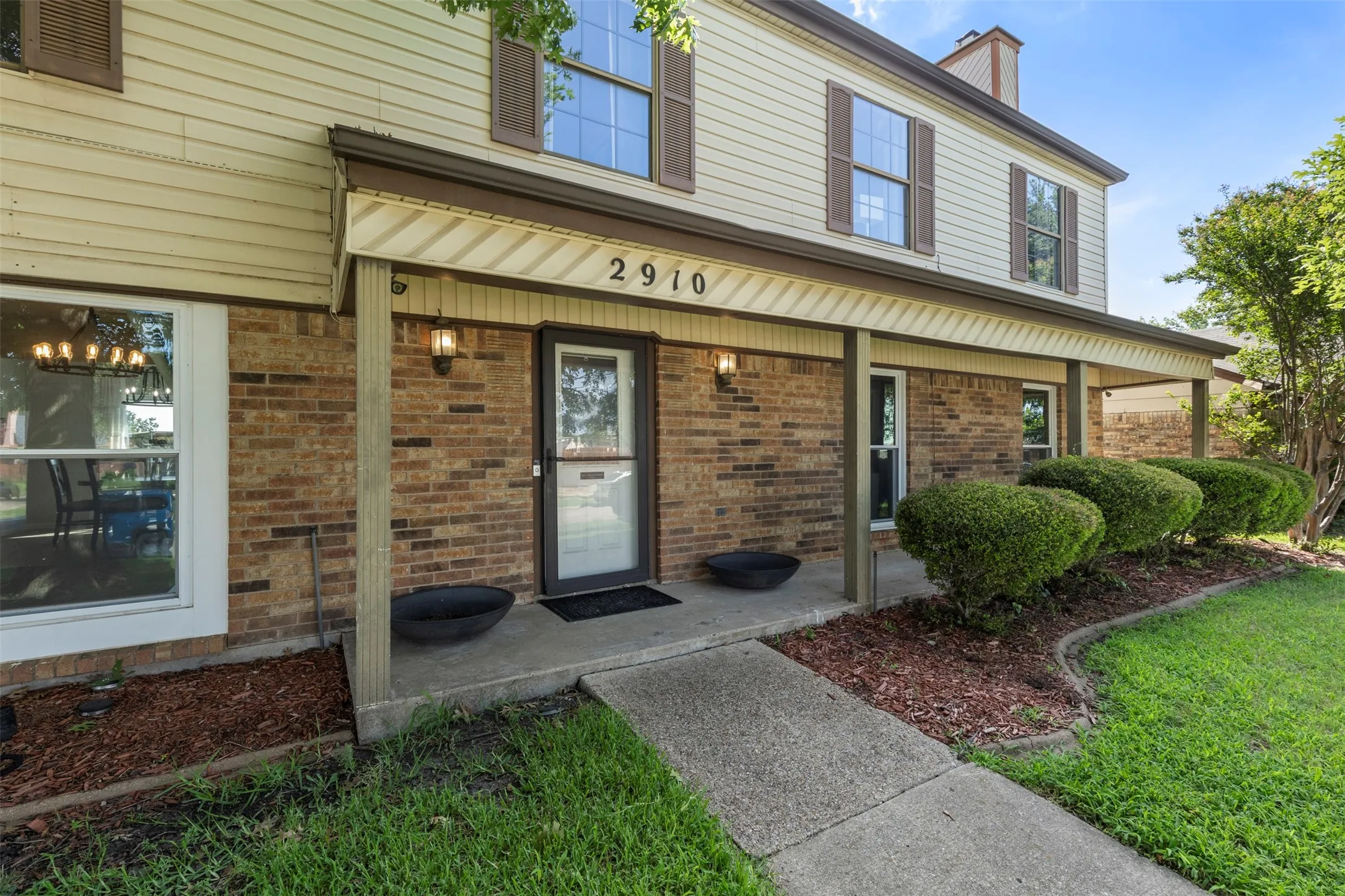 Two-story residence featuring a brick and siding exterior, covered front porch, and established landscaping