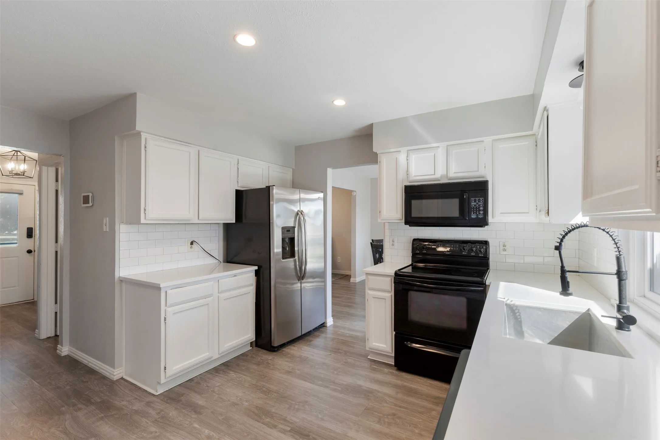 Kitchen featuring white cabinetry, light-toned countertops, a stainless steel refrigerator, black range, and black microwave