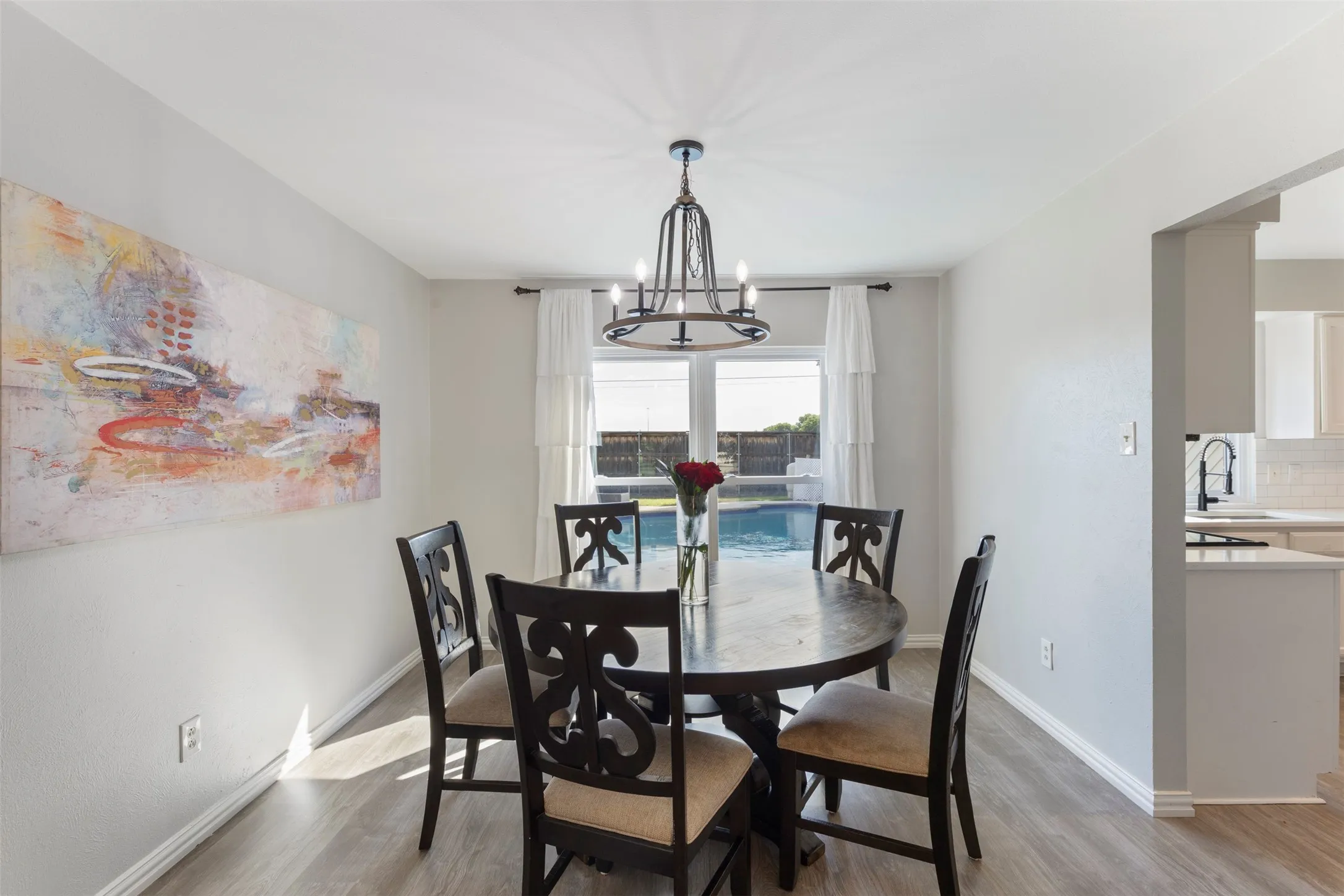 Dining area featuring wood-finish flooring, a contemporary chandelier, and a large window overlooking a backyard pool