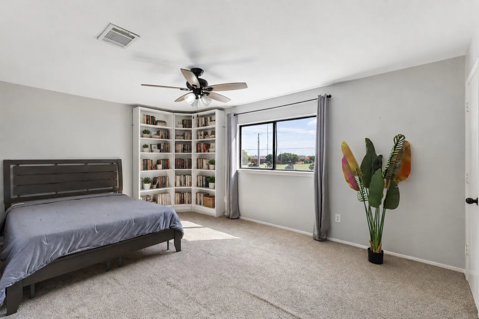 Spacious room featuring light-colored carpet flooring, a corner built-in bookcase, and a ceiling fan with integrated lighting