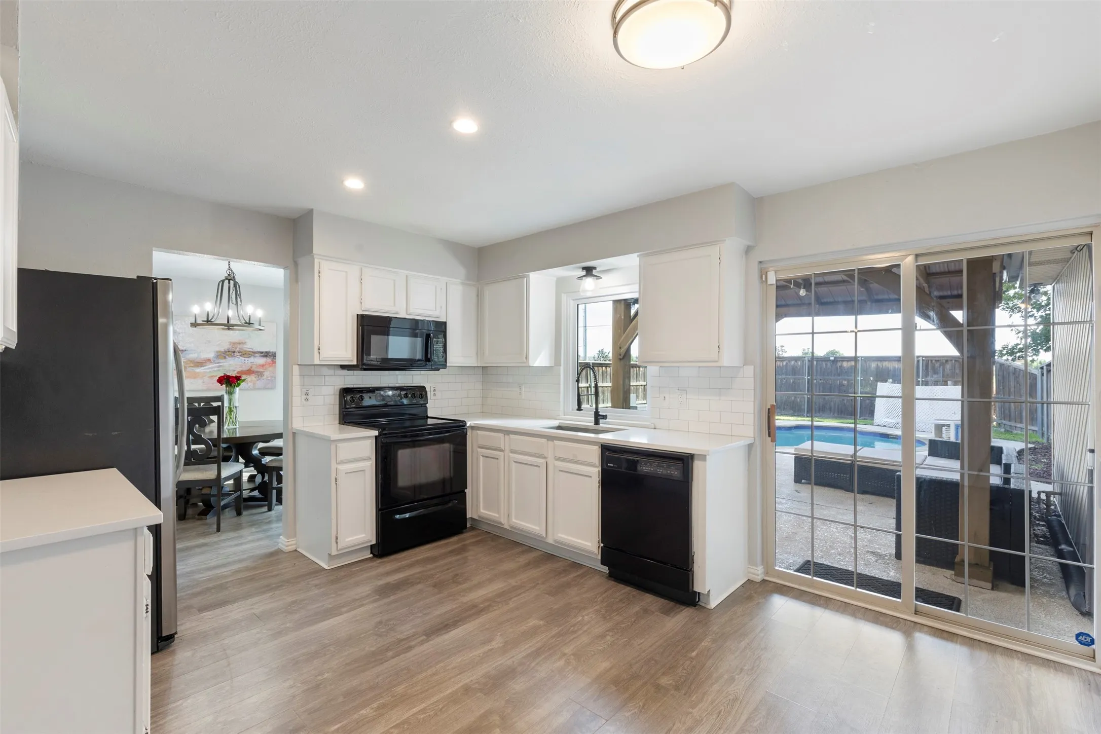 Kitchen featuring wood-finish flooring, white cabinetry, black appliances, subway tile backsplash, and sliding glass doors opening to an outdoor pool