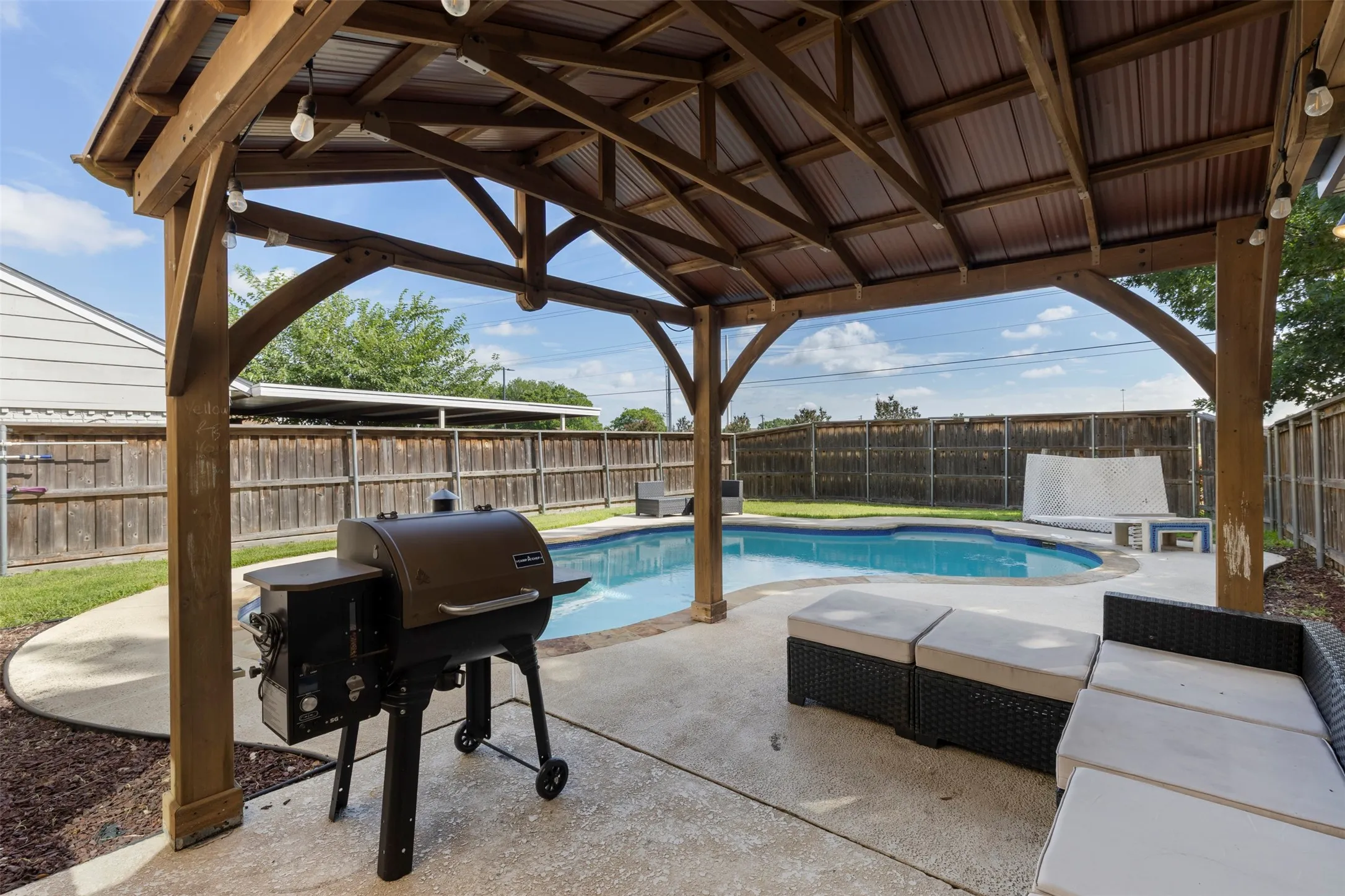 Outdoor entertainment area featuring a wood-frame gazebo with a corrugated metal roof and string lighting