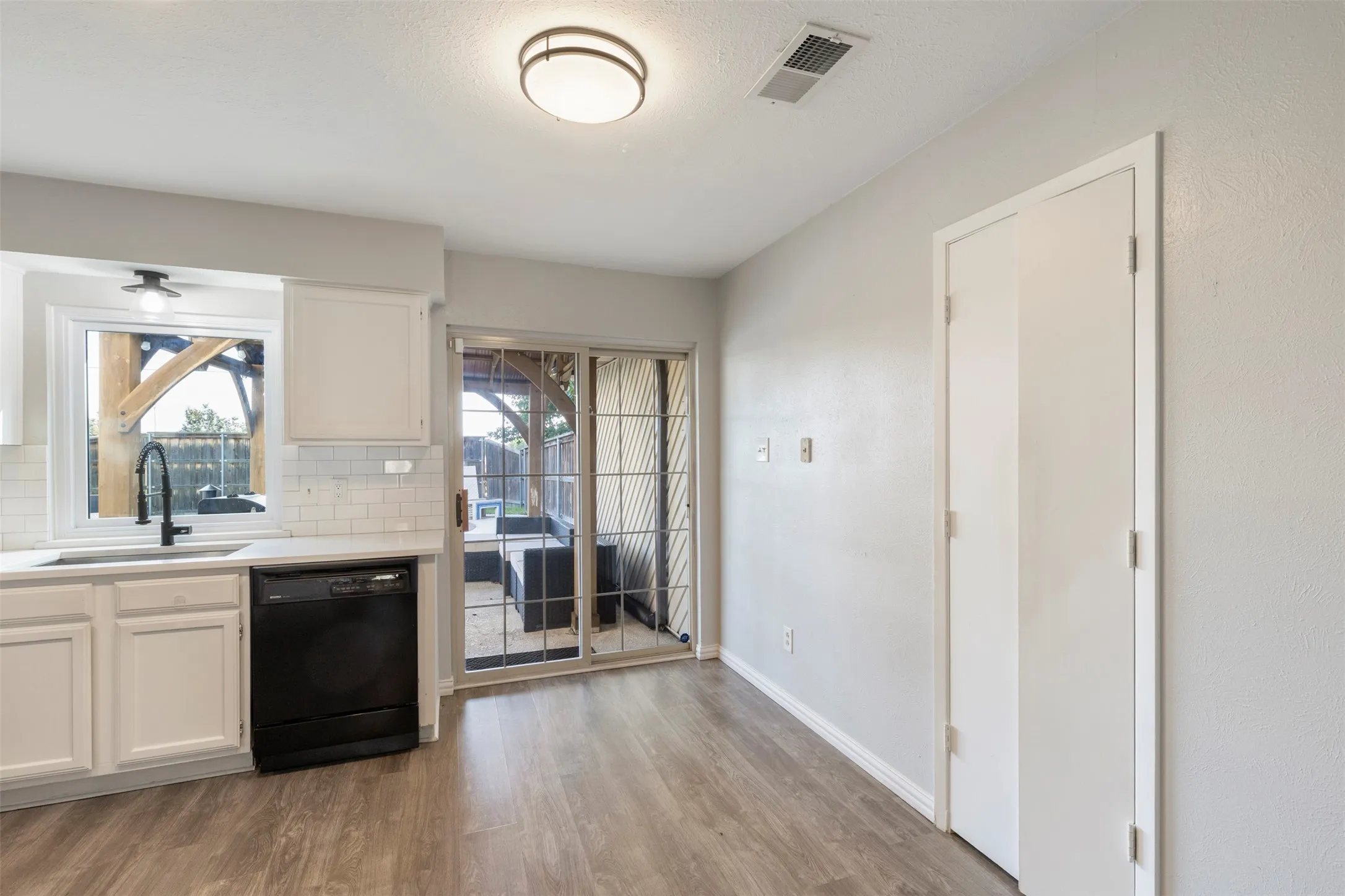 Kitchen area featuring white cabinetry, a black dishwasher, and a white subway tile backsplash