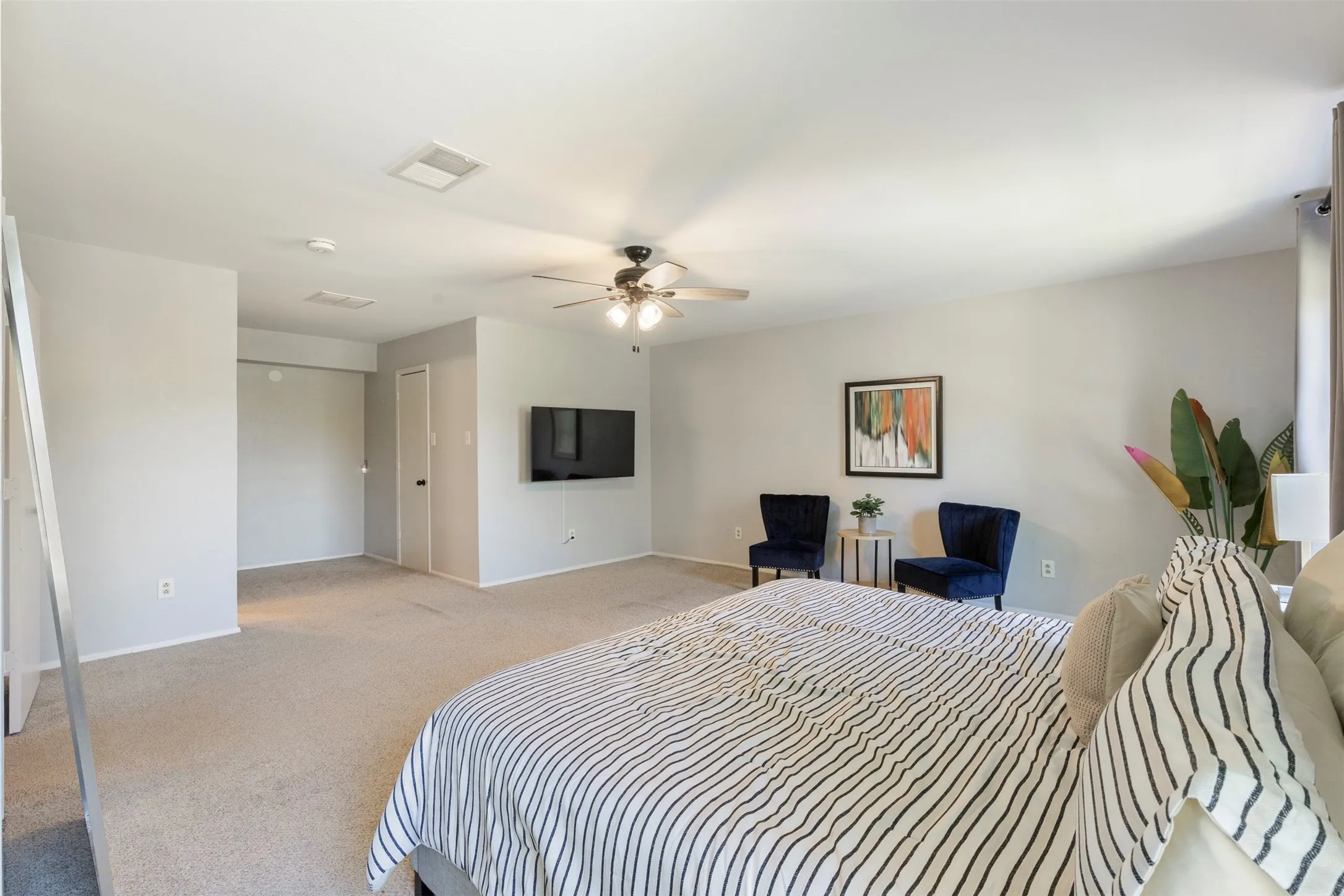 Spacious carpeted room featuring a ceiling fan with light fixture, light gray wall paint, and white trim