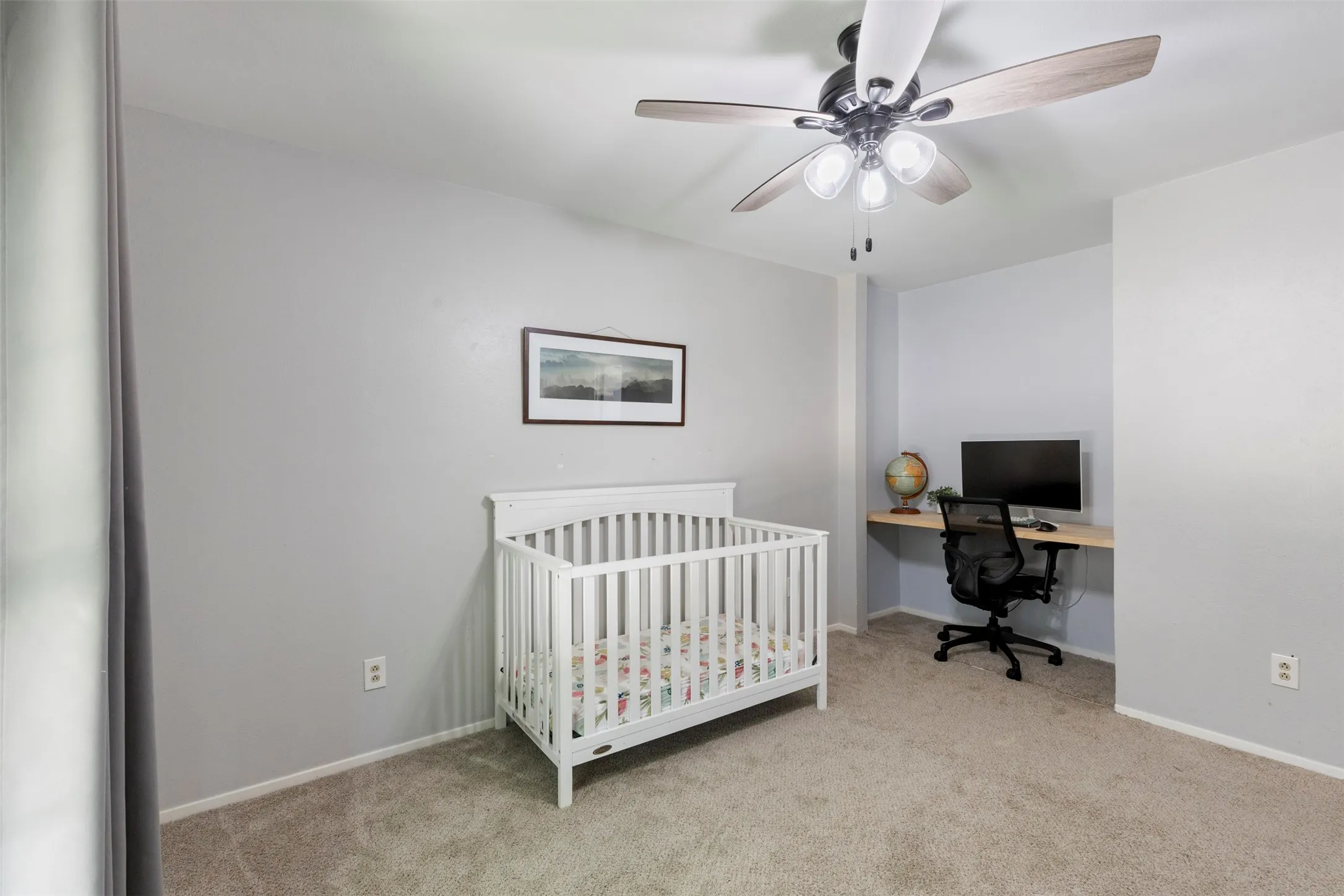 Carpeted room featuring a ceiling fan with light fixture, built-in floating desk, and light gray wall paint