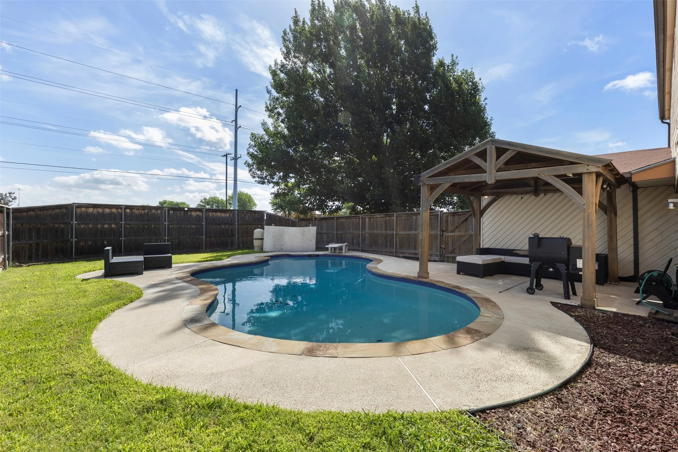 Curved inground pool with concrete decking, surrounded by a wood privacy fence