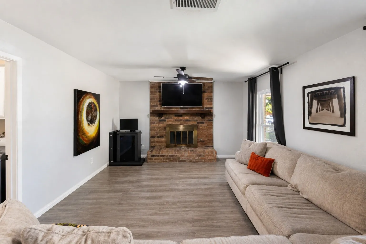 Living area featuring a brick fireplace with a brass firebox, ceiling fan, and wood-finish flooring