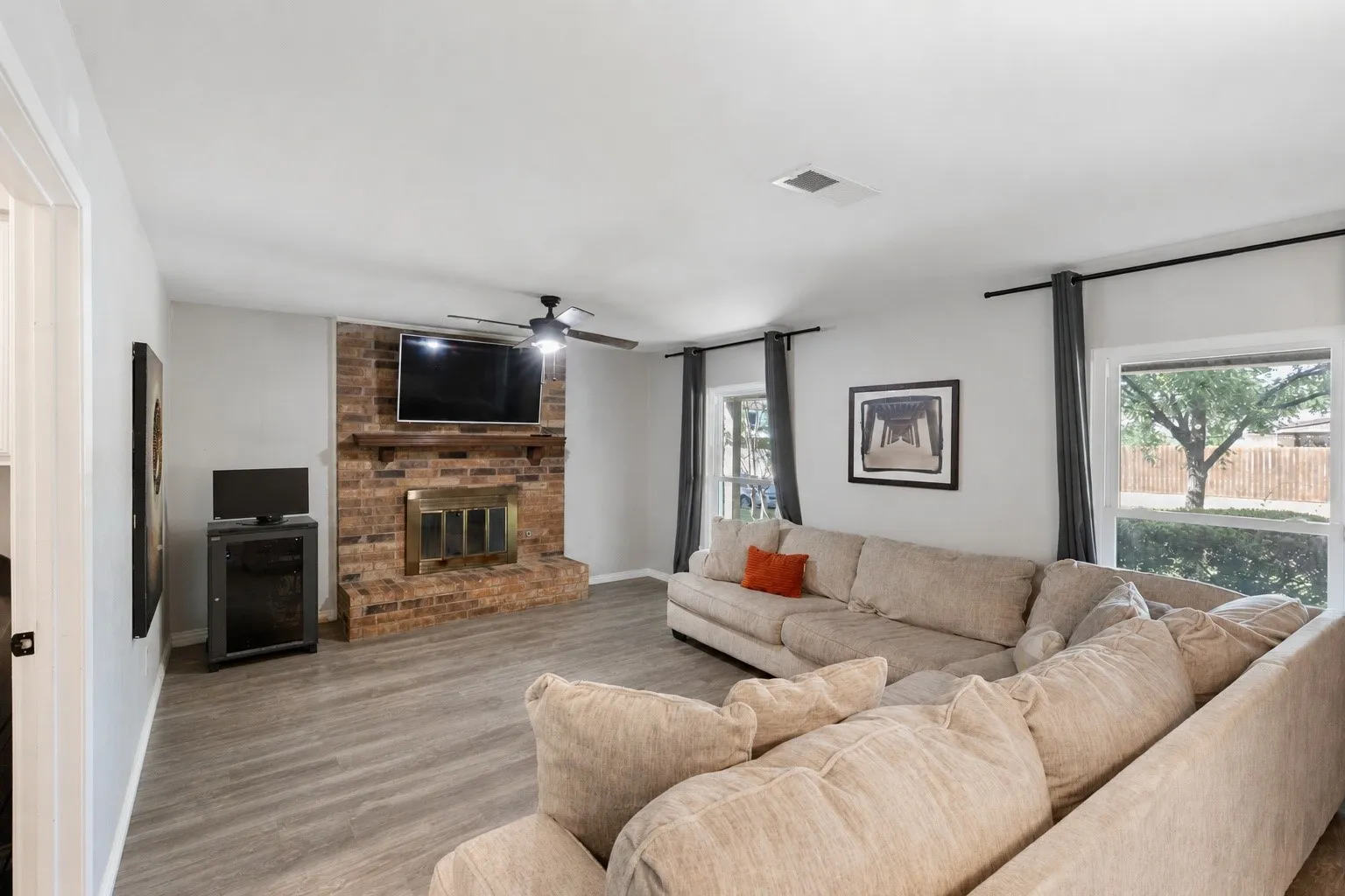 Spacious living area featuring a brick fireplace with a wood mantle, wood-finish flooring, and a ceiling fan