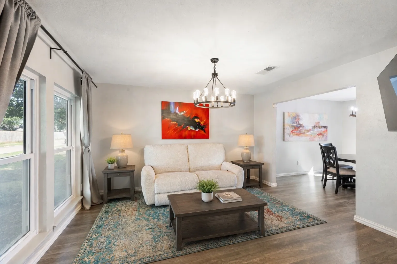 Spacious living area featuring wood-finish flooring, white walls, and a contemporary chandelier