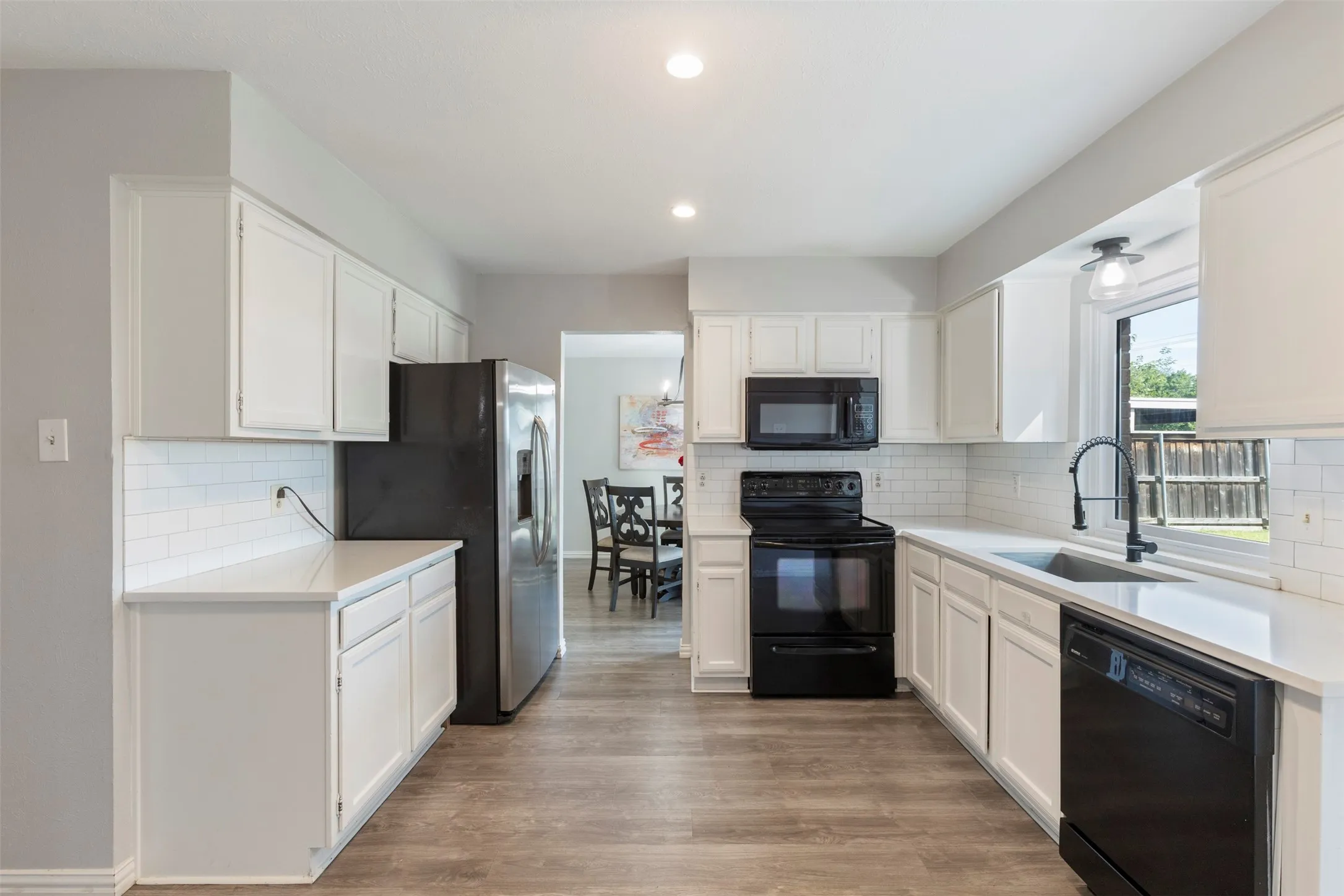 Kitchen featuring white cabinetry, light countertops, wood-finish flooring, subway tile backsplash, and black appliances