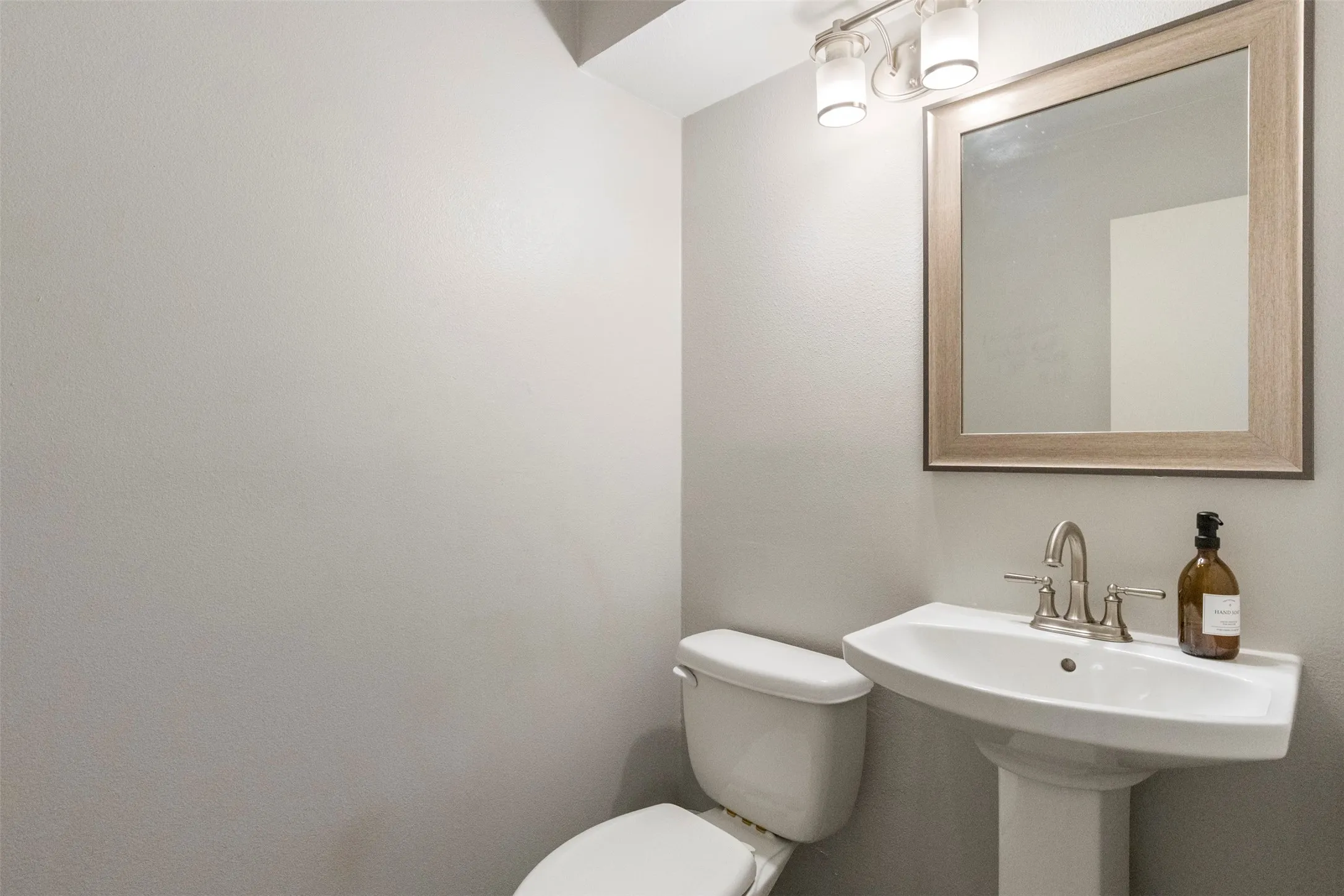 Pedestal sink with brushed nickel faucet, framed mirror, and dual-bulb vanity lighting