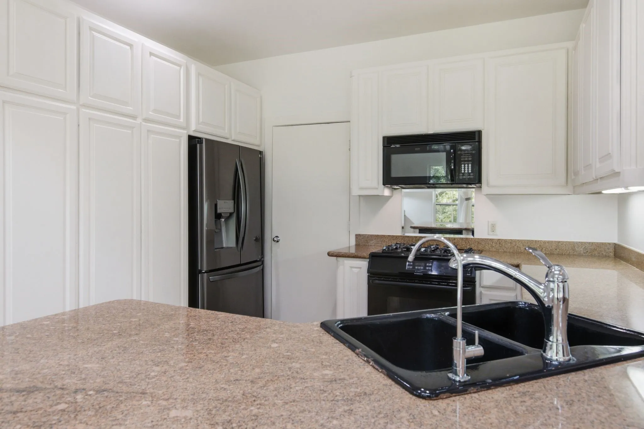 Kitchen featuring extensive white cabinetry, a black appliance suite, and light-toned stone countertops