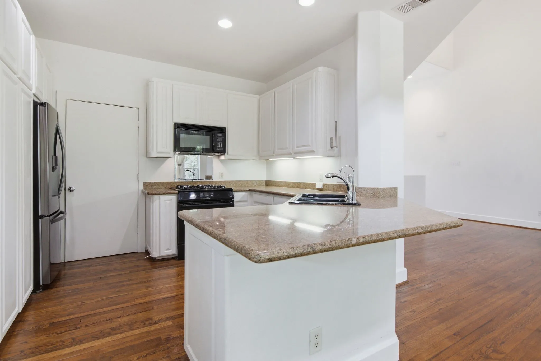 Kitchen featuring wood-finish flooring, white cabinetry, undermount sink with a gooseneck faucet, black appliances, and speckled countertops
