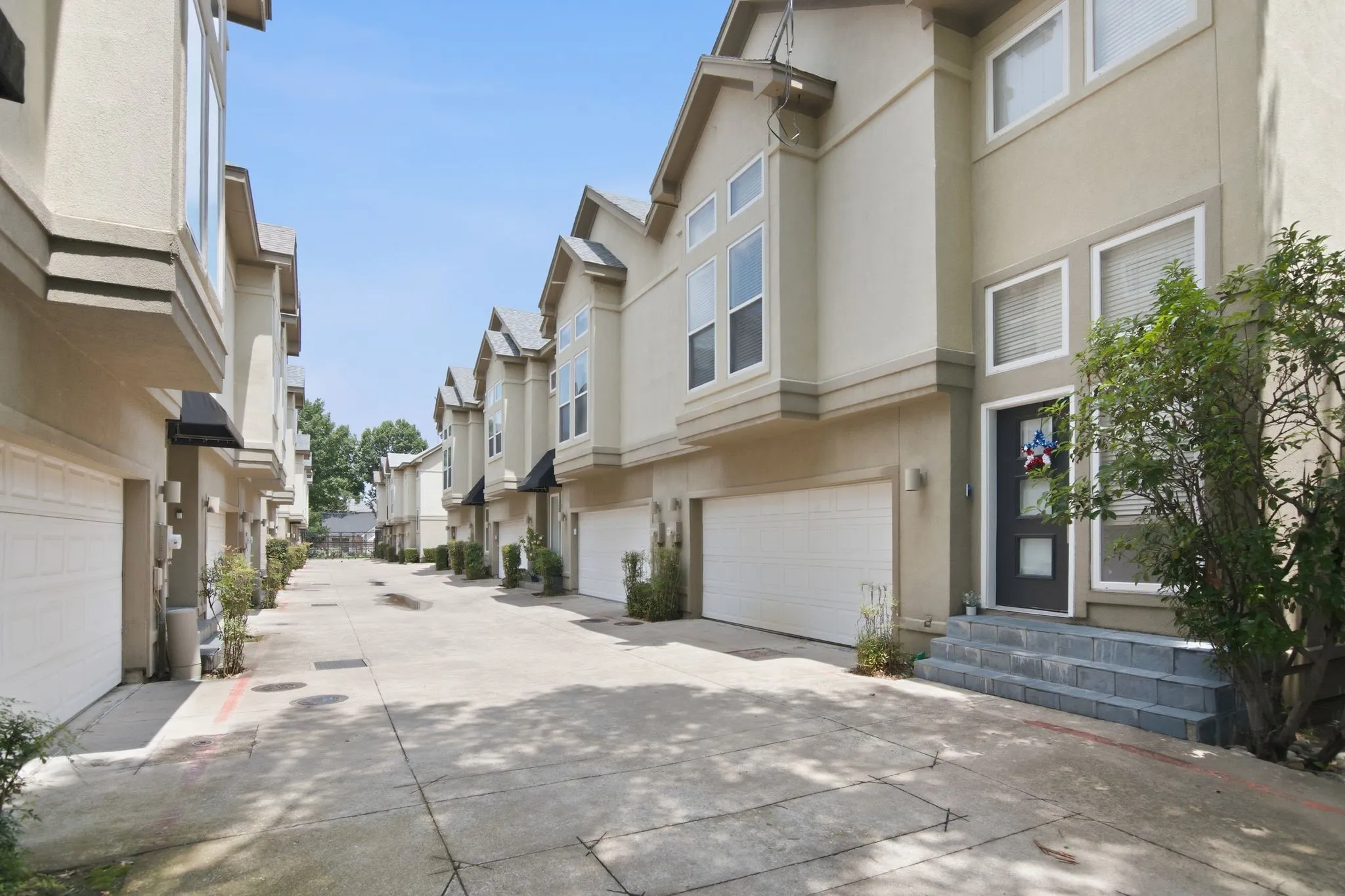 Contemporary stucco townhome featuring an integrated garage, prominent bay windows, a dark paneled entry door, and multi-paned windows