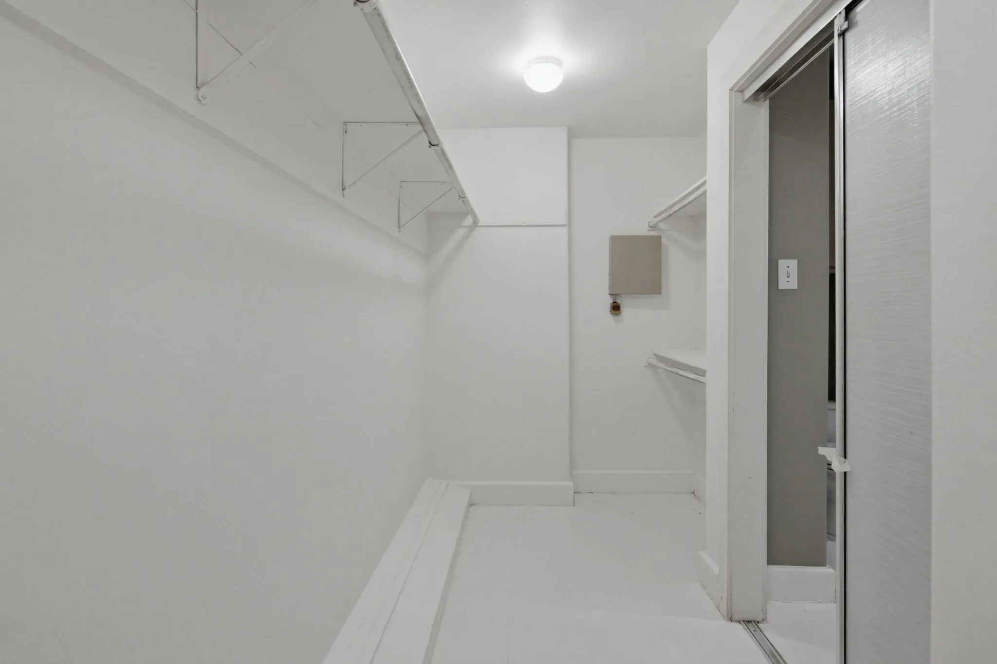 Brightly lit closet space featuring a white color palette, suspended clothing rods, built-in shelving, a flush mount ceiling fixture, and a sliding door