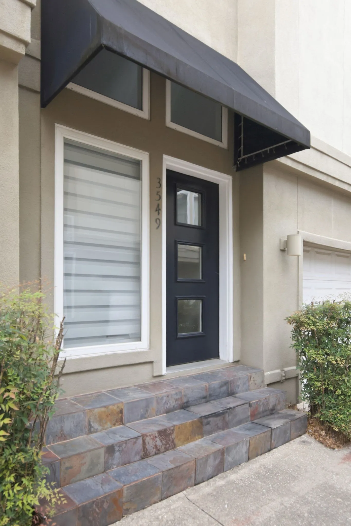 Contemporary 2 tone stucco townhome featuring an integrated garage, prominent bay windows, a dark paneled entry door, and multi-paned windows