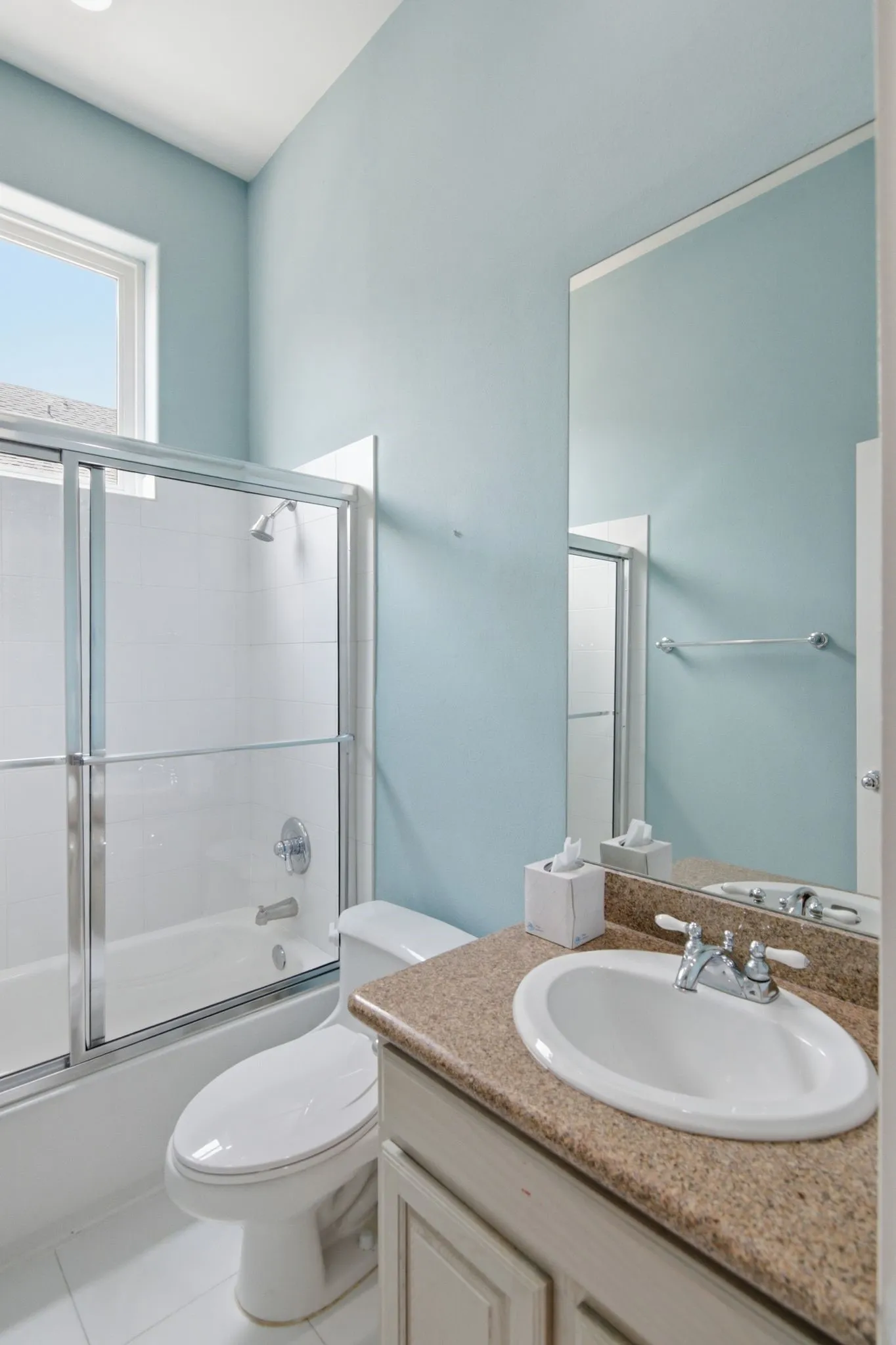 Full bathroom featuring a shower-tub combination with sliding glass doors, a single vanity with a stone-finish countertop, and a built-in mirror