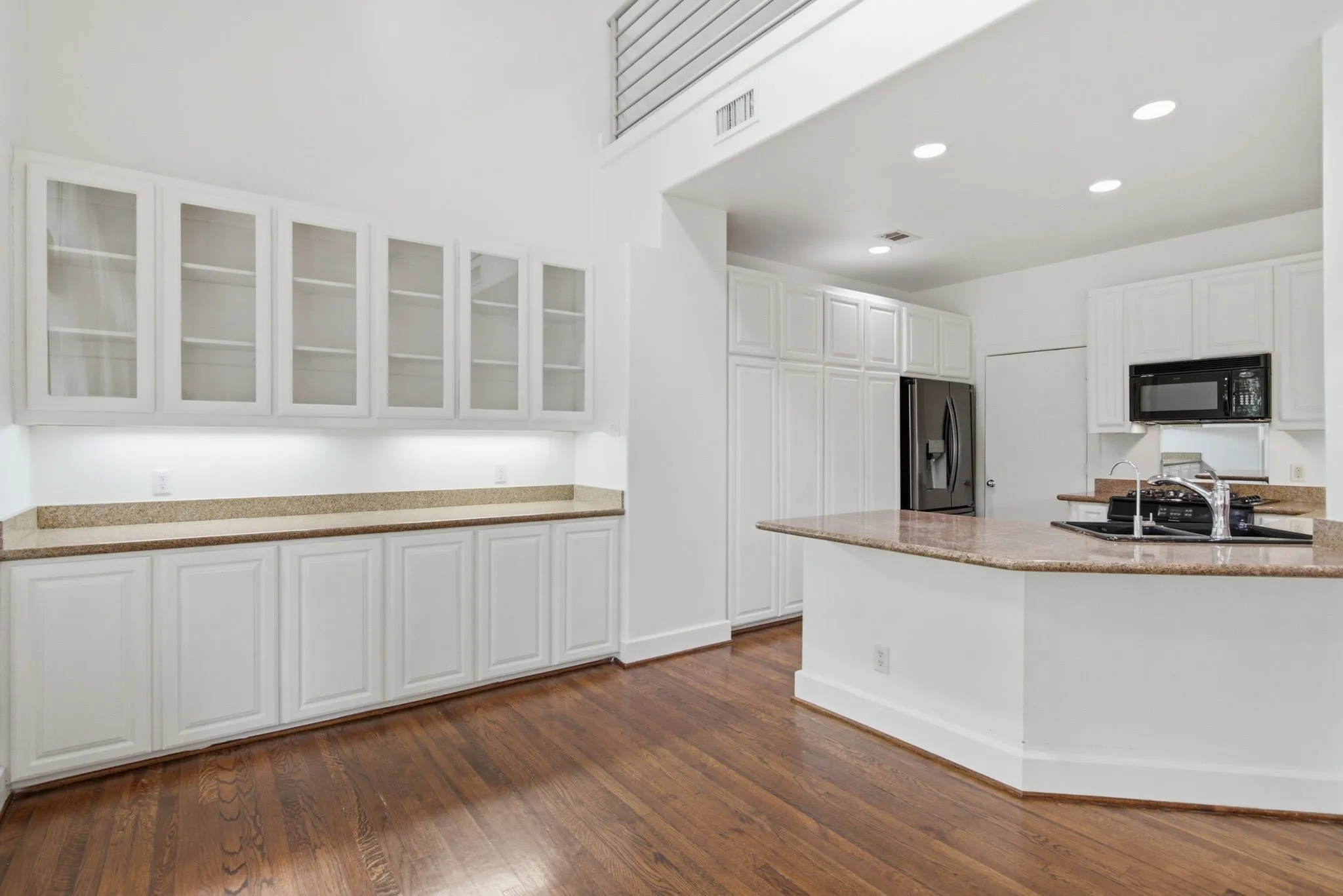 Open-concept kitchen and dining area featuring rich wood-finish flooring, white cabinetry, granite countertops, and recessed lighting