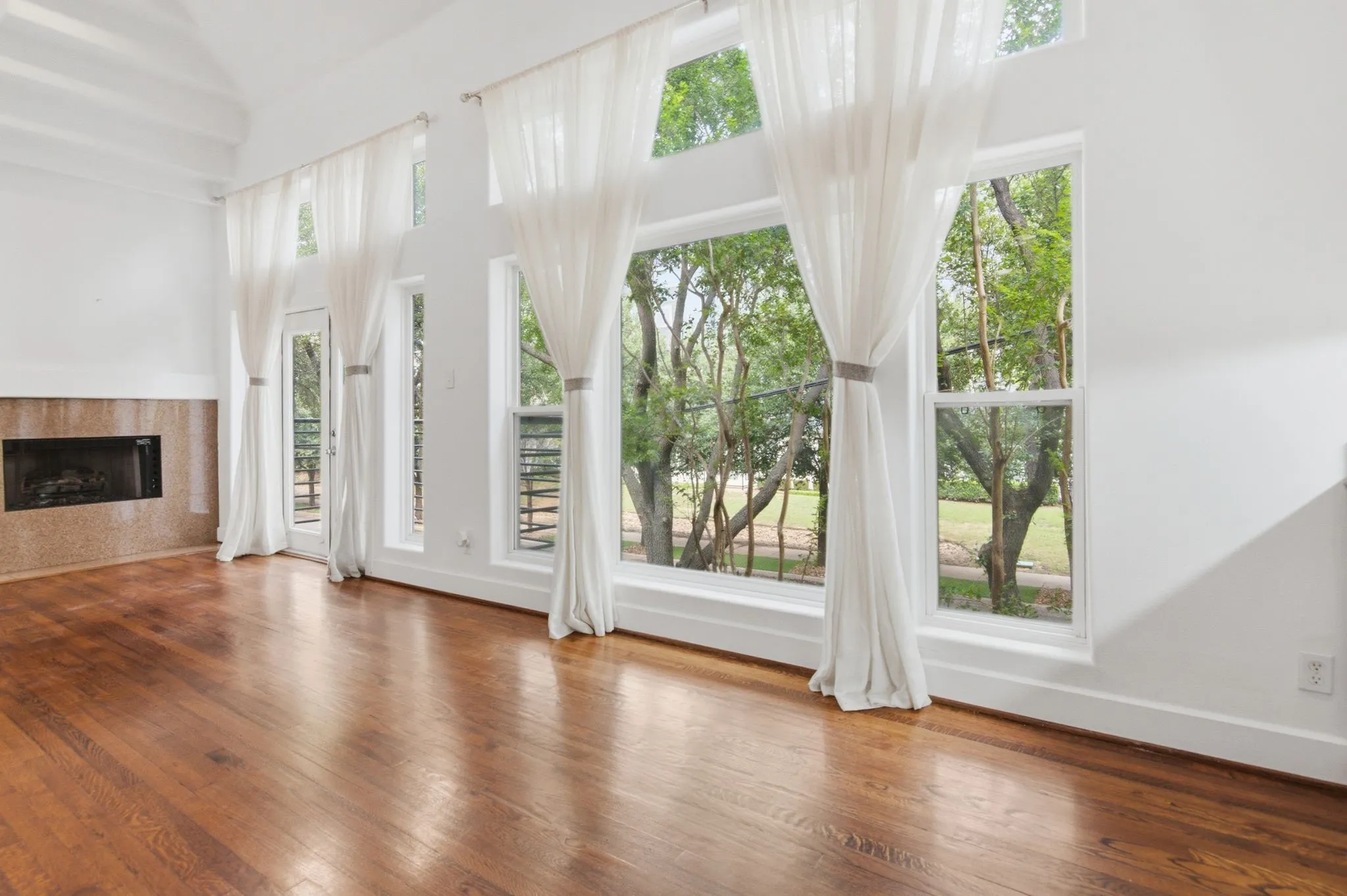 Living space featuring expansive windows, wood-finish flooring, a contemporary fireplace with a stone surround, high ceilings, and a glass-paneled door