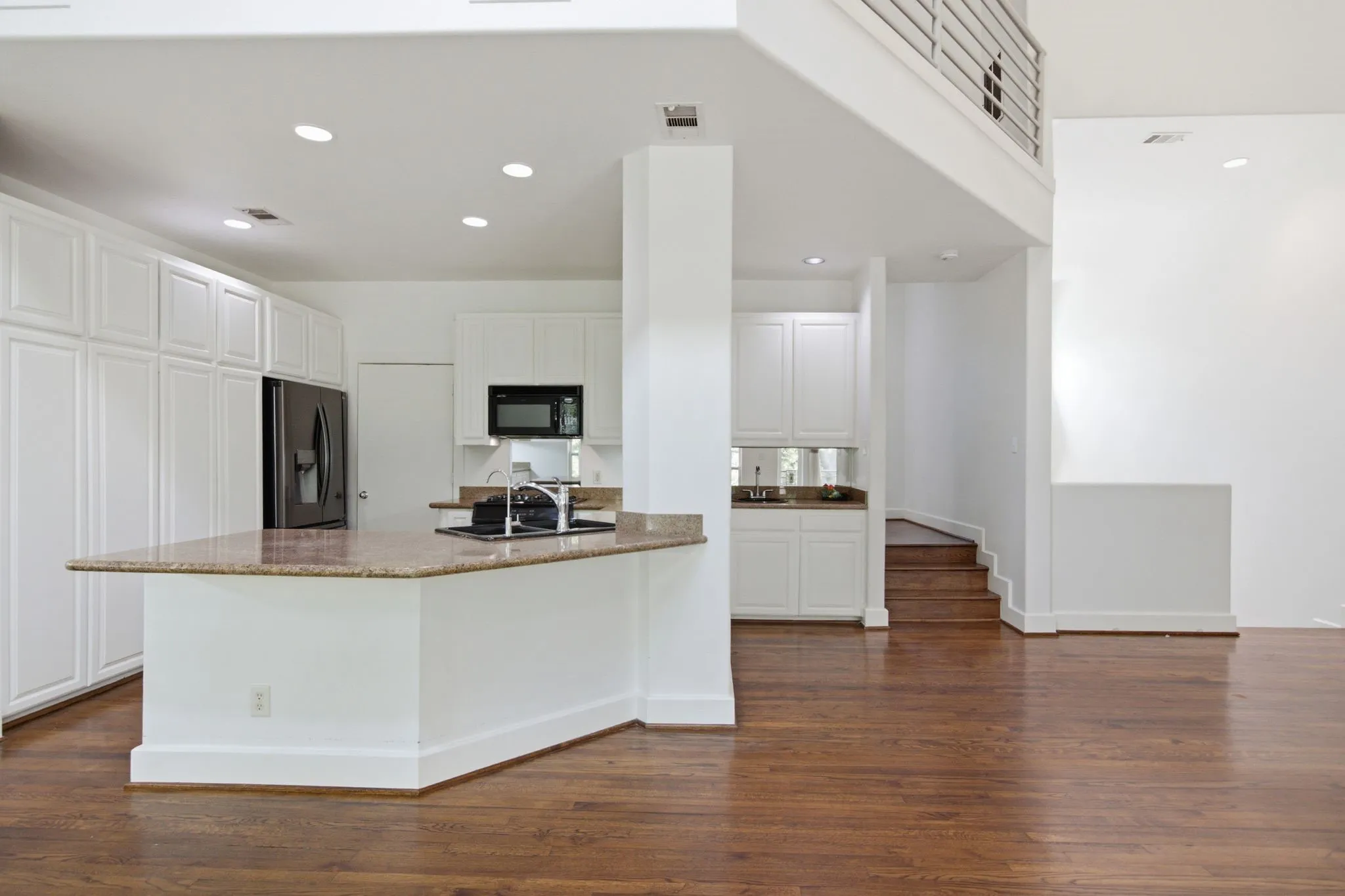 Open-concept kitchen featuring a granite-topped island, white cabinetry, dark wood-finish flooring, a stainless steel refrigerator, and recessed lighting