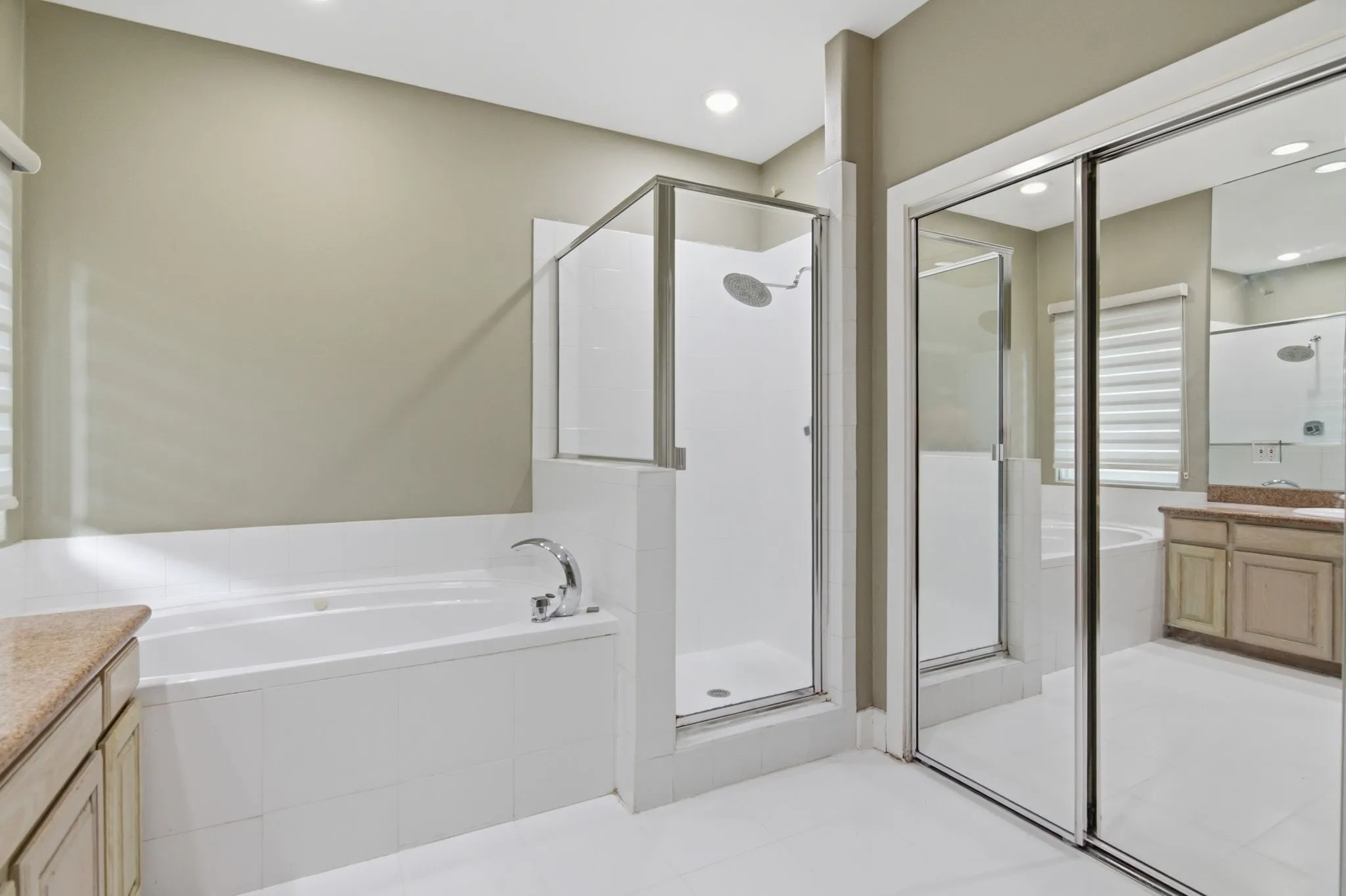 Bathroom featuring a built-in soaking tub with chrome fixtures, a glass-enclosed standing shower with a rain shower head, and sliding mirrored closet doors