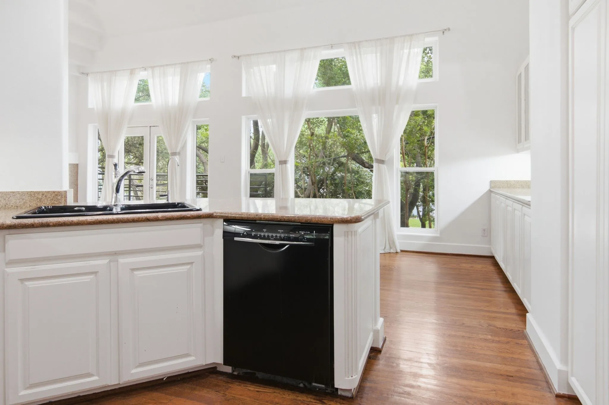 Kitchen featuring a black undermount sink, granite countertops, white cabinetry, and a black dishwasher