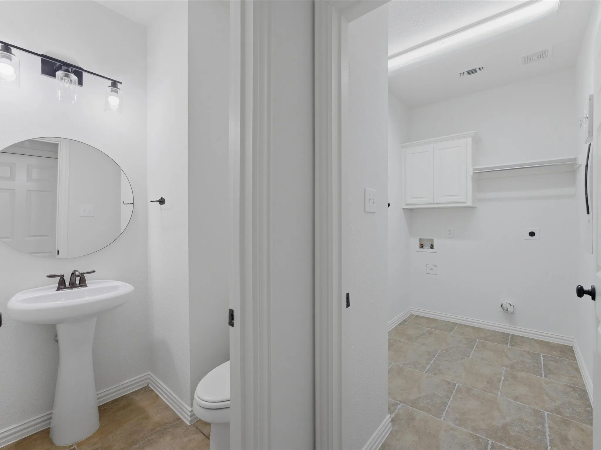 Pedestal sink with an oval mirror and a three-light vanity fixture