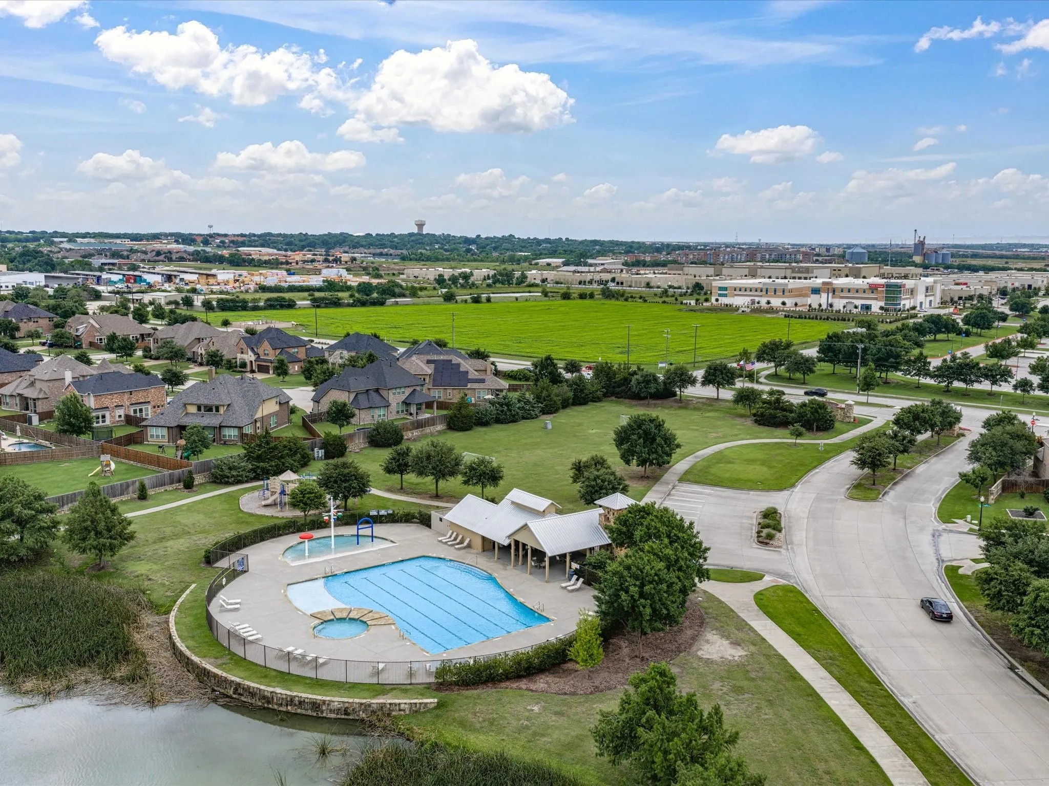 Community swimming pool with a connected spa and covered seating area, bordered by a tranquil pond