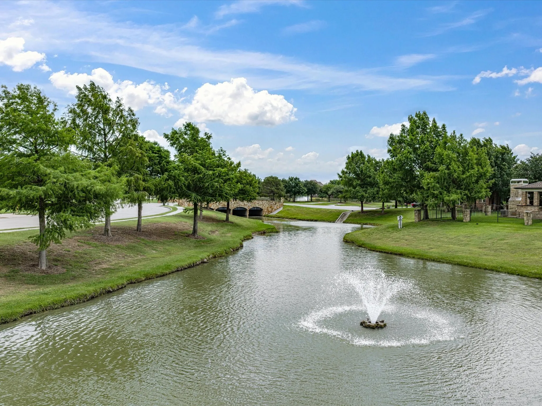 Water feature with a decorative fountain, surrounded by manicured green spaces and mature trees