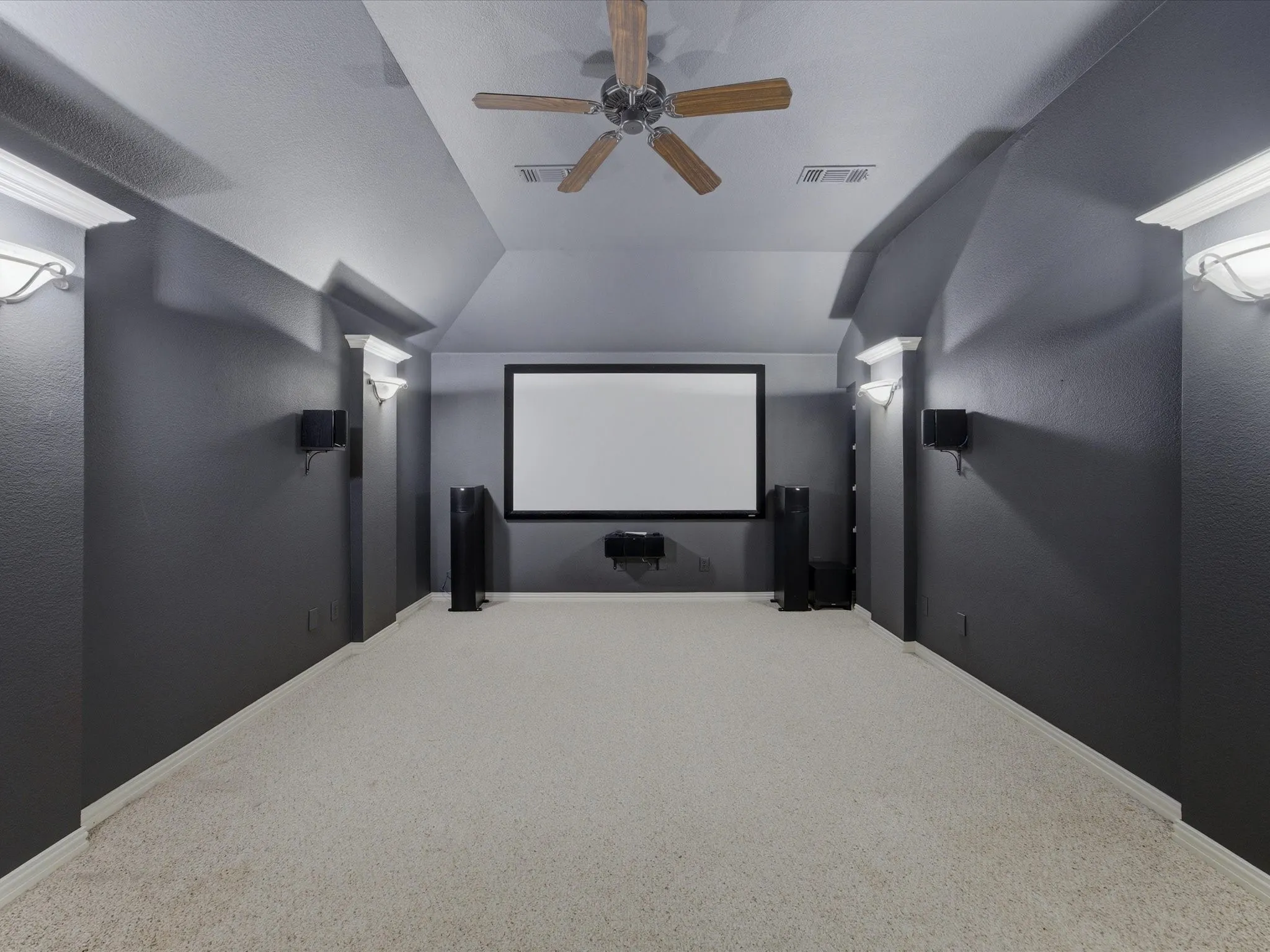 Dedicated media room featuring a large projector screen, dark accent walls, and recessed lighting