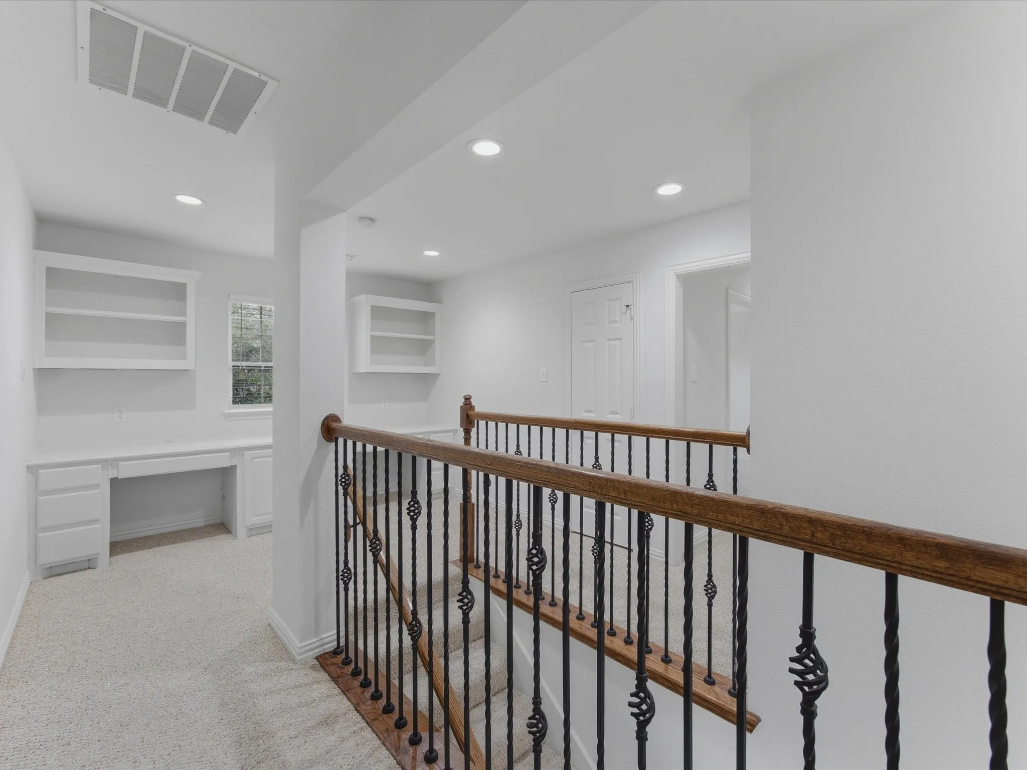Staircase with wrought iron balusters and wood handrail, featuring recessed lighting, built-in desks, and custom shelving