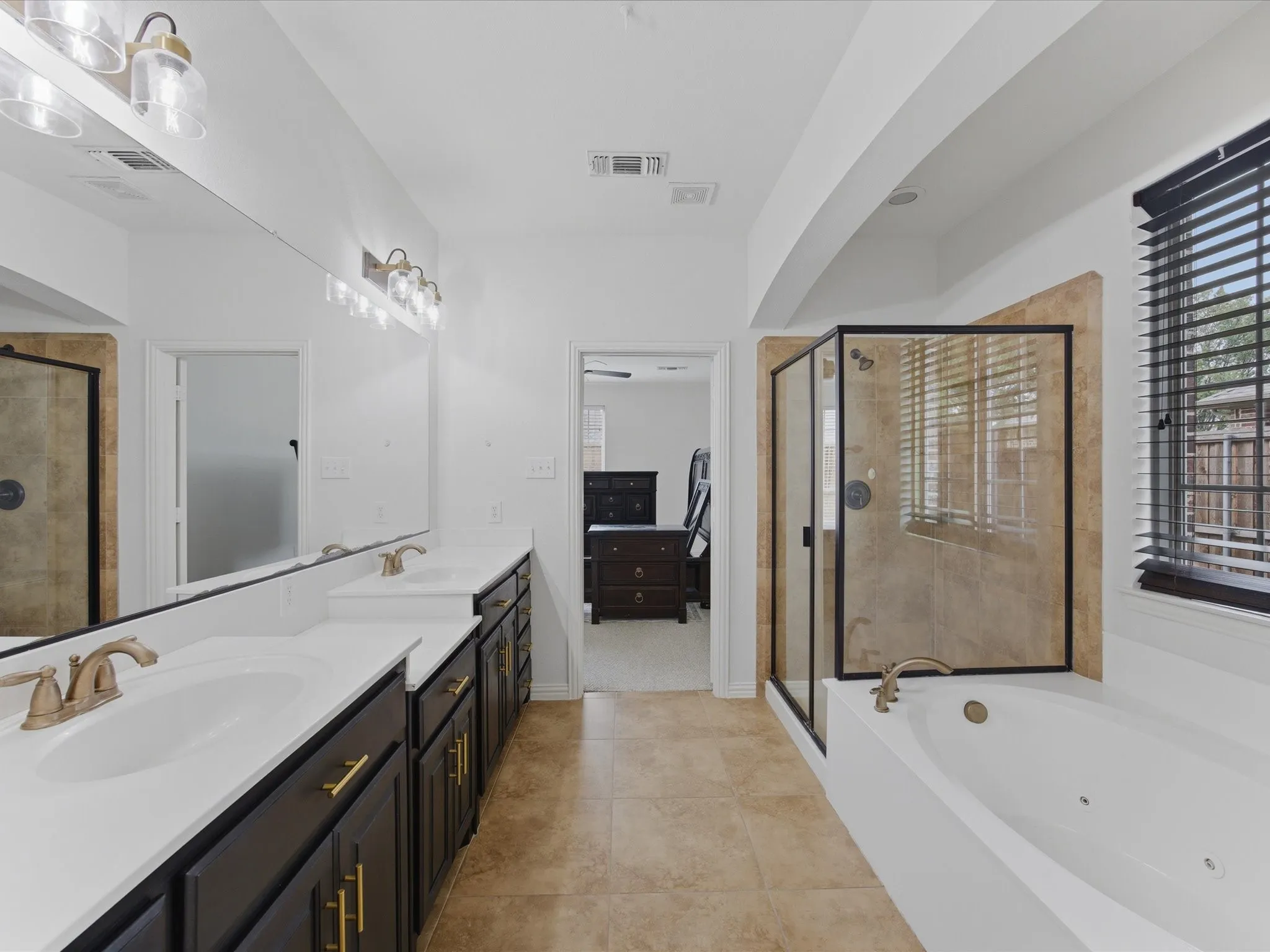 Primary Bathroom featuring dual vanities with white countertops, dark wood cabinetry, and gold-finish hardware