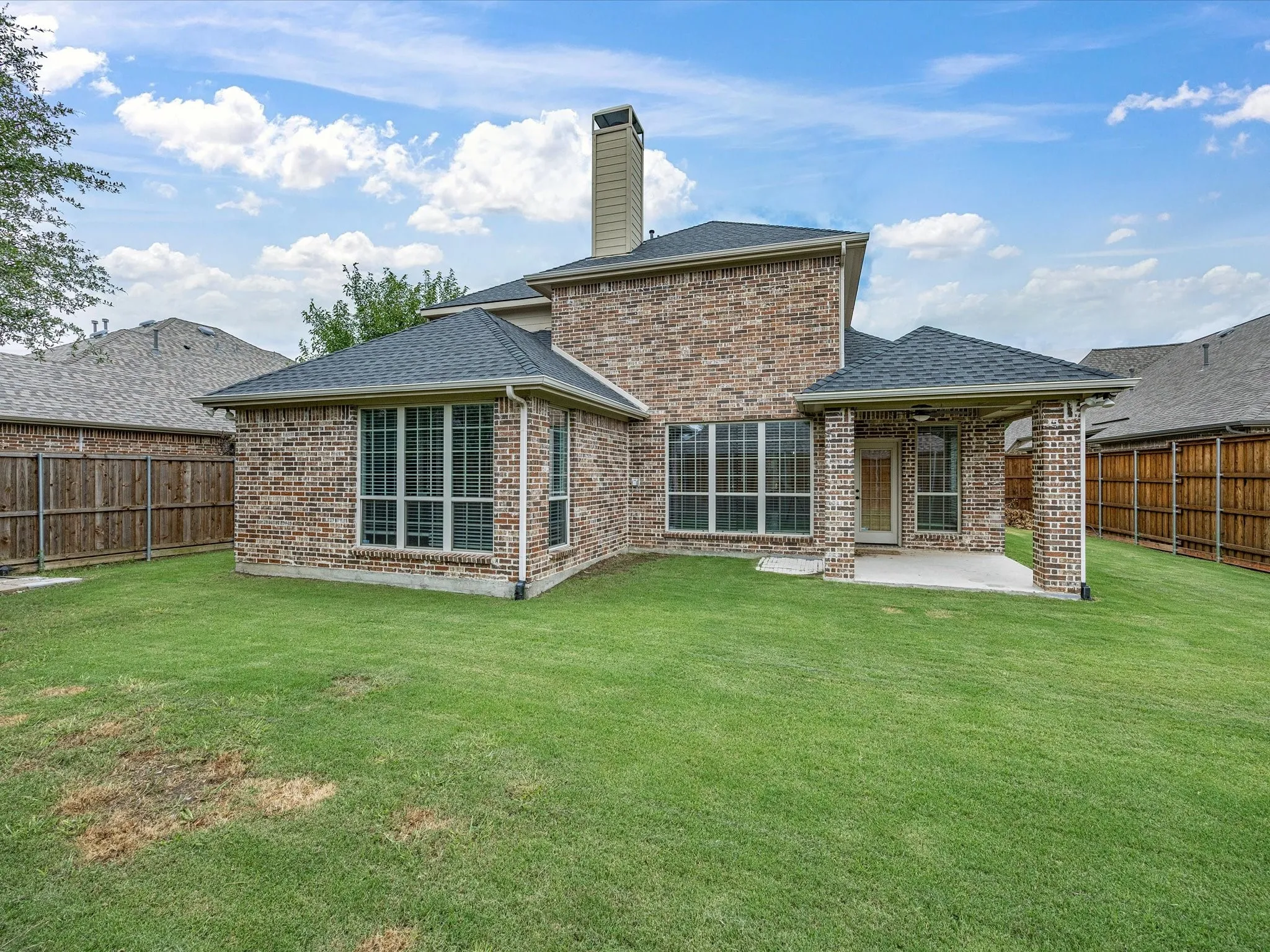 Expansive backyard featuring a manicured lawn, full brick exterior, a covered patio with a ceiling fan, multiple large windows, and a prominent chimney