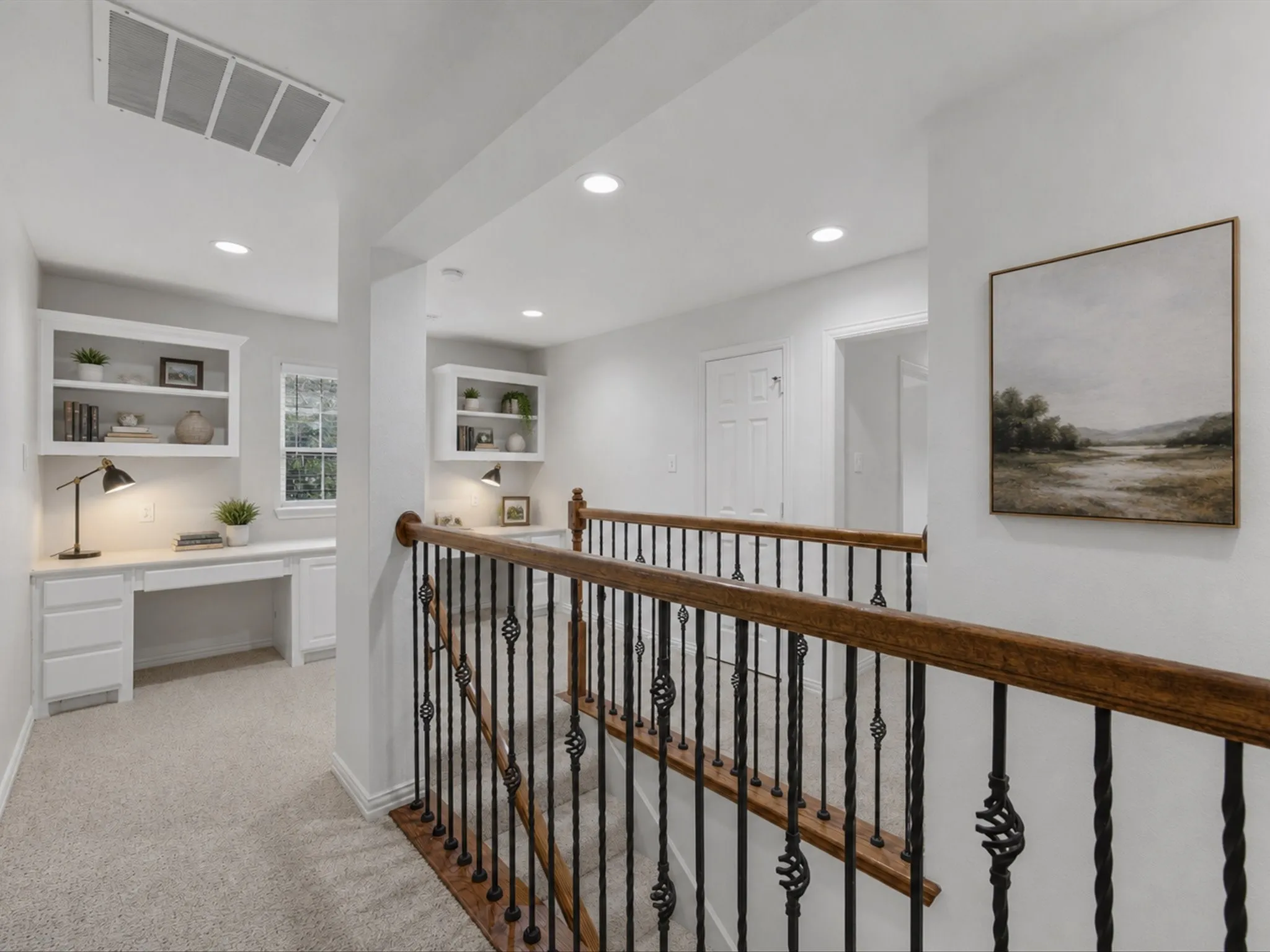 Virtually staged second-story landing featuring built-in desks with shelving, recessed lighting, and a staircase with wrought iron balusters and a wood-finish handrail