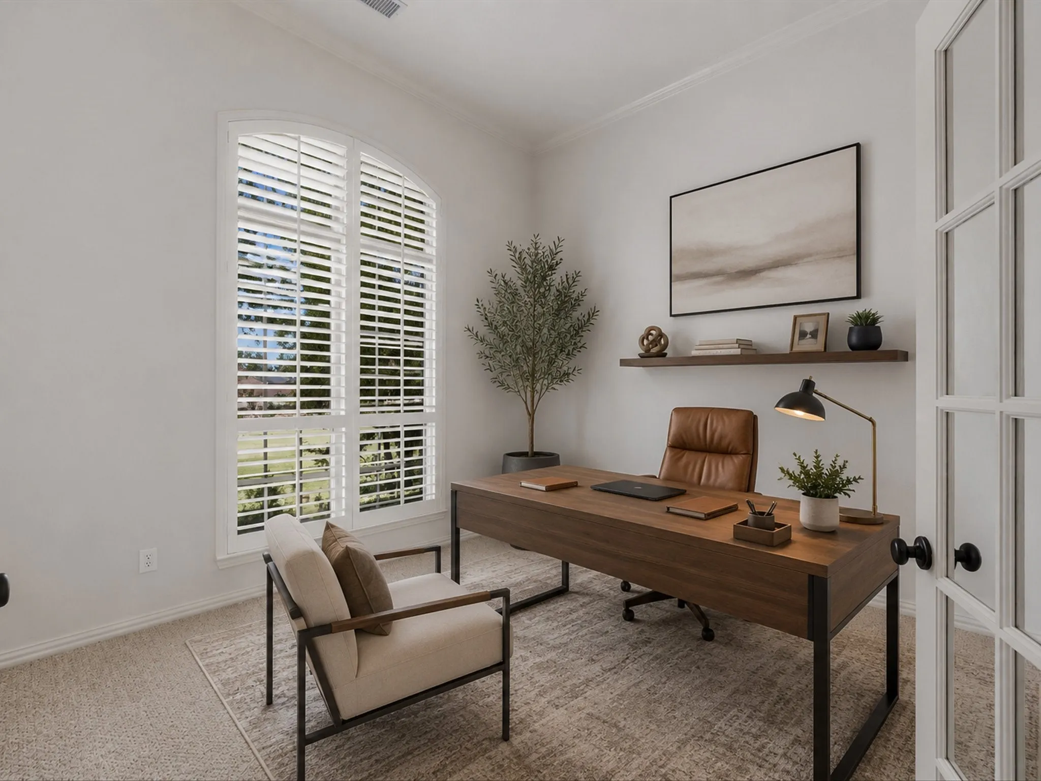 Virtually staged Office featuring an arched window with plantation shutters, crown molding, light-colored carpeting, a floating wood shelf, and French doors with matte black hardware