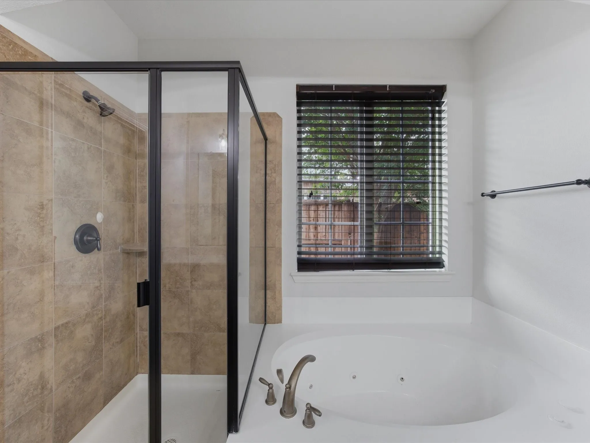 Primary Bathroom featuring a deep soaking tub with deck-mounted fixtures, a separate shower with a glass enclosure and tiled surround, and a window with horizontal blinds