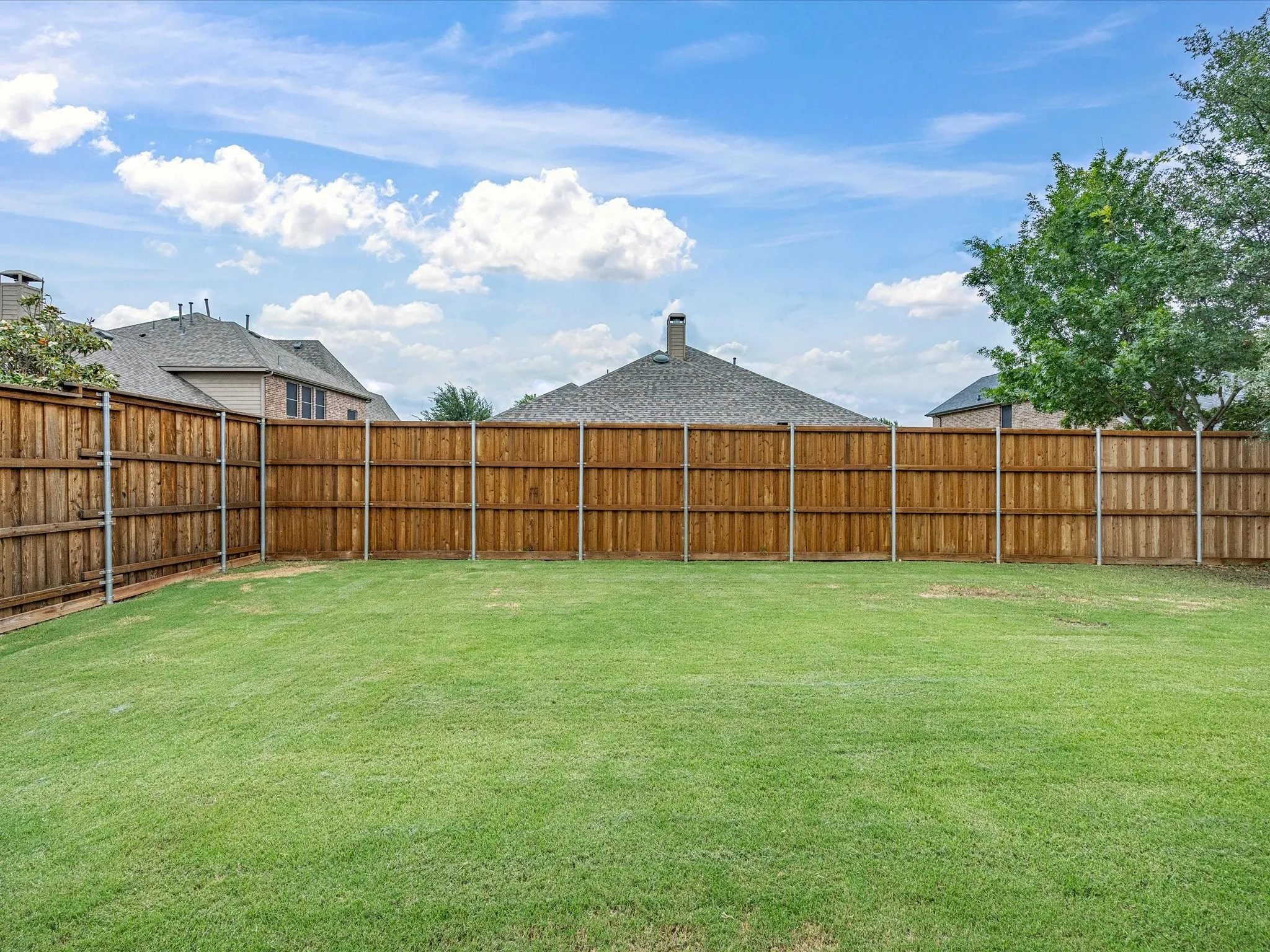 Expansive backyard featuring a manicured lawn, full wood-plank fencing, and mature perimeter trees