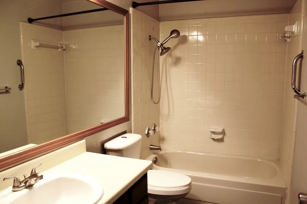 Built-in bathtub with subway tile surround, chrome shower fixtures, vanity with integrated sink, and framed wall mirror